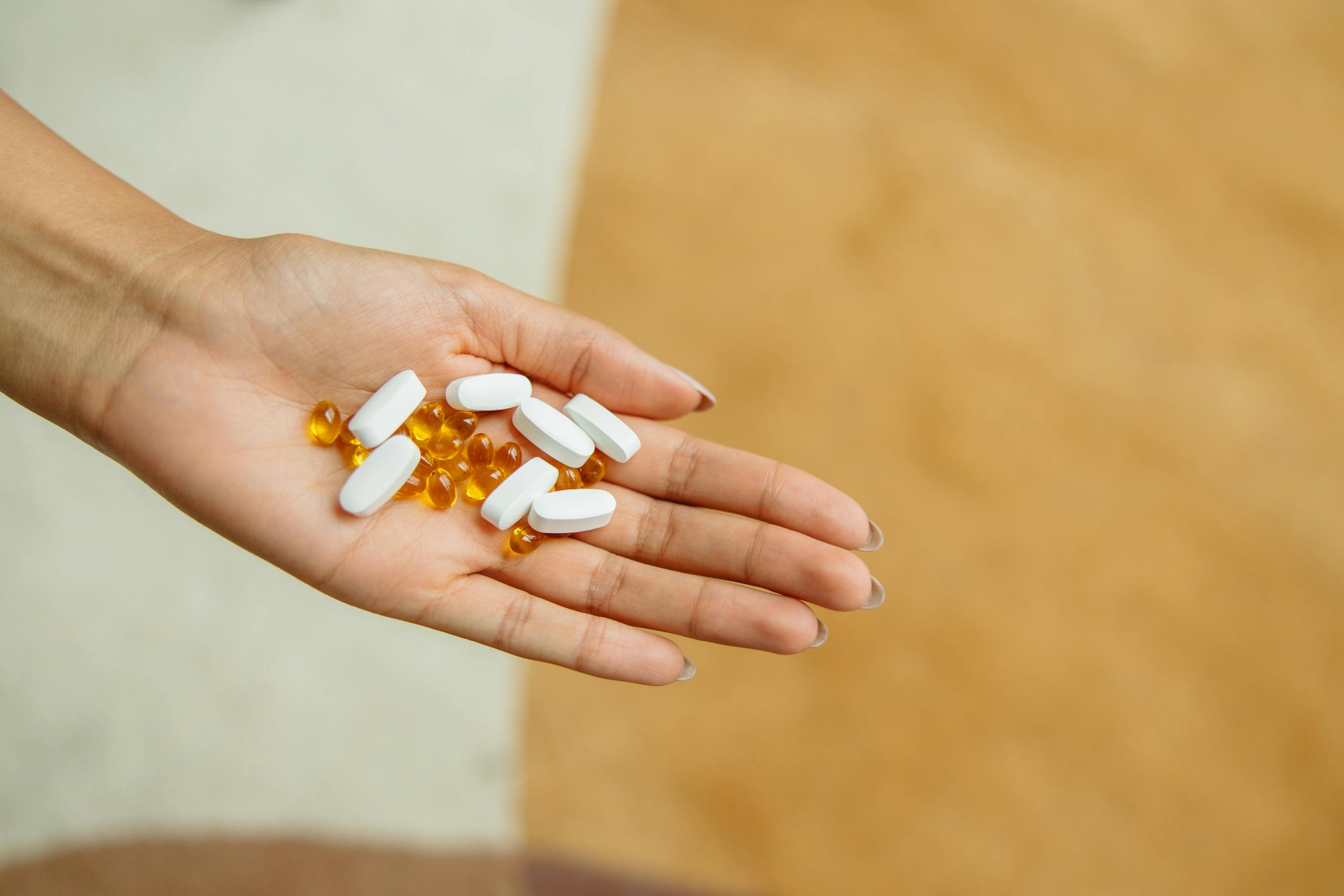 Close-up of a hand holding white pills and yellow capsules, symbolizing health and wellness.