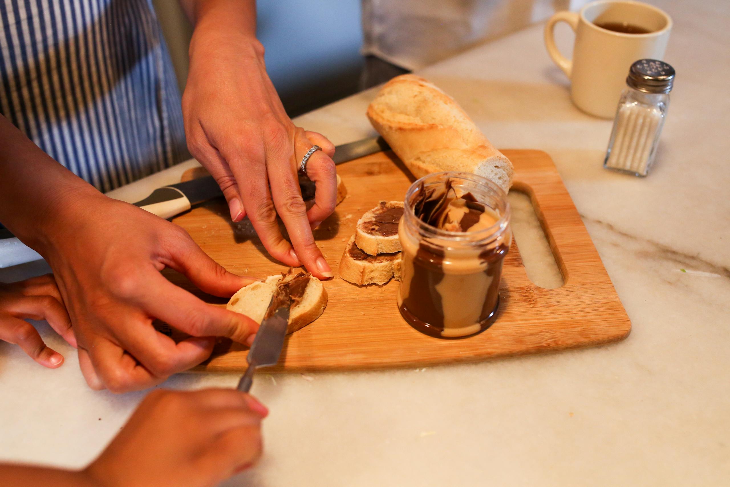 Close-up of a mother and child making peanut butter toast in the kitchen.