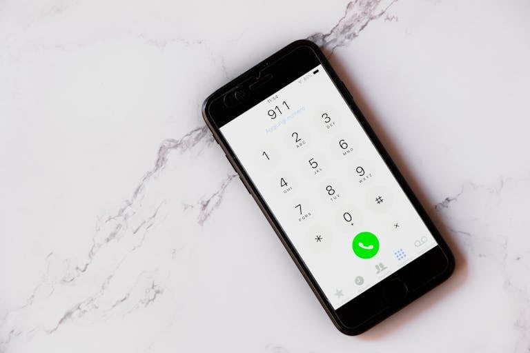 Close-up of a smartphone displaying the emergency number 911 on a white marble surface.