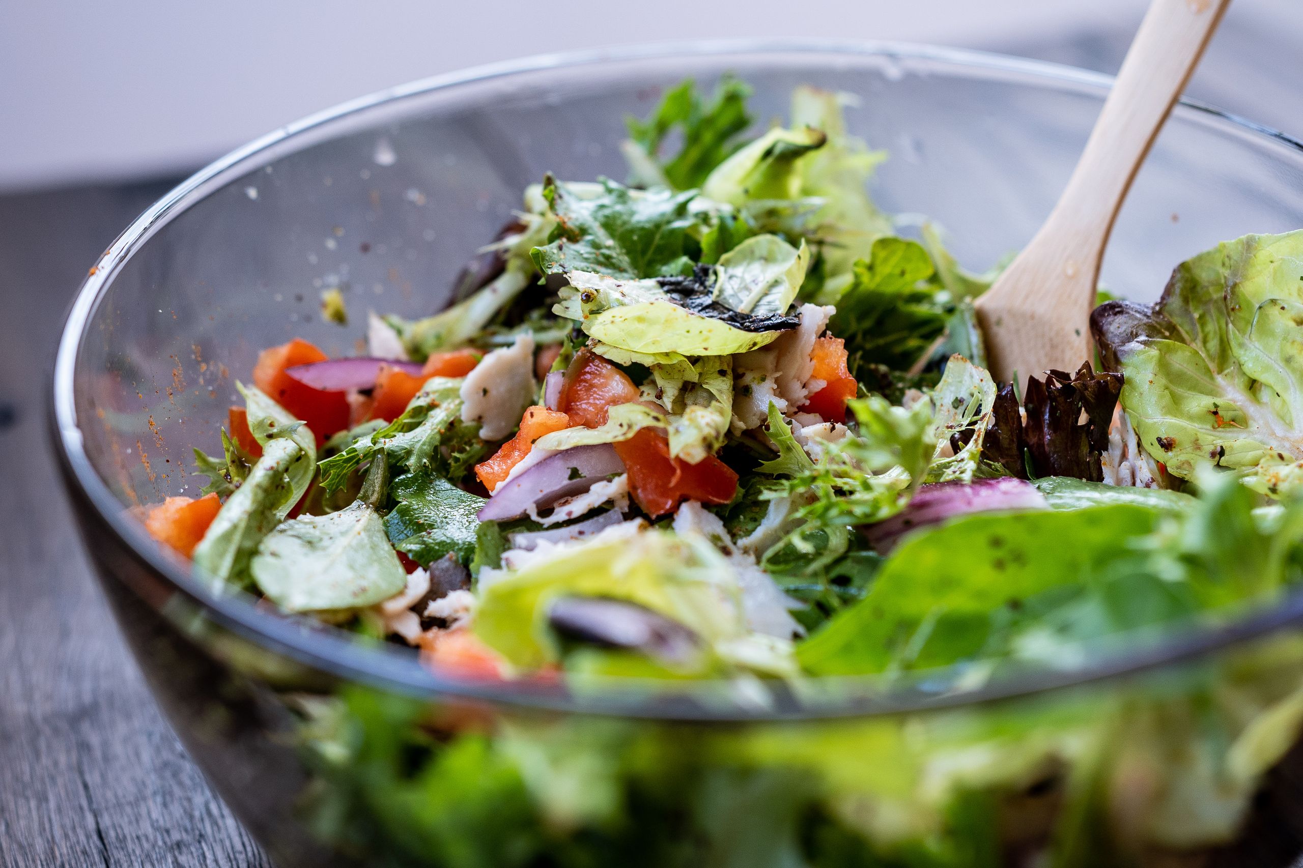 Close-up of a vibrant fresh salad in a glass bowl with a wooden spatula.