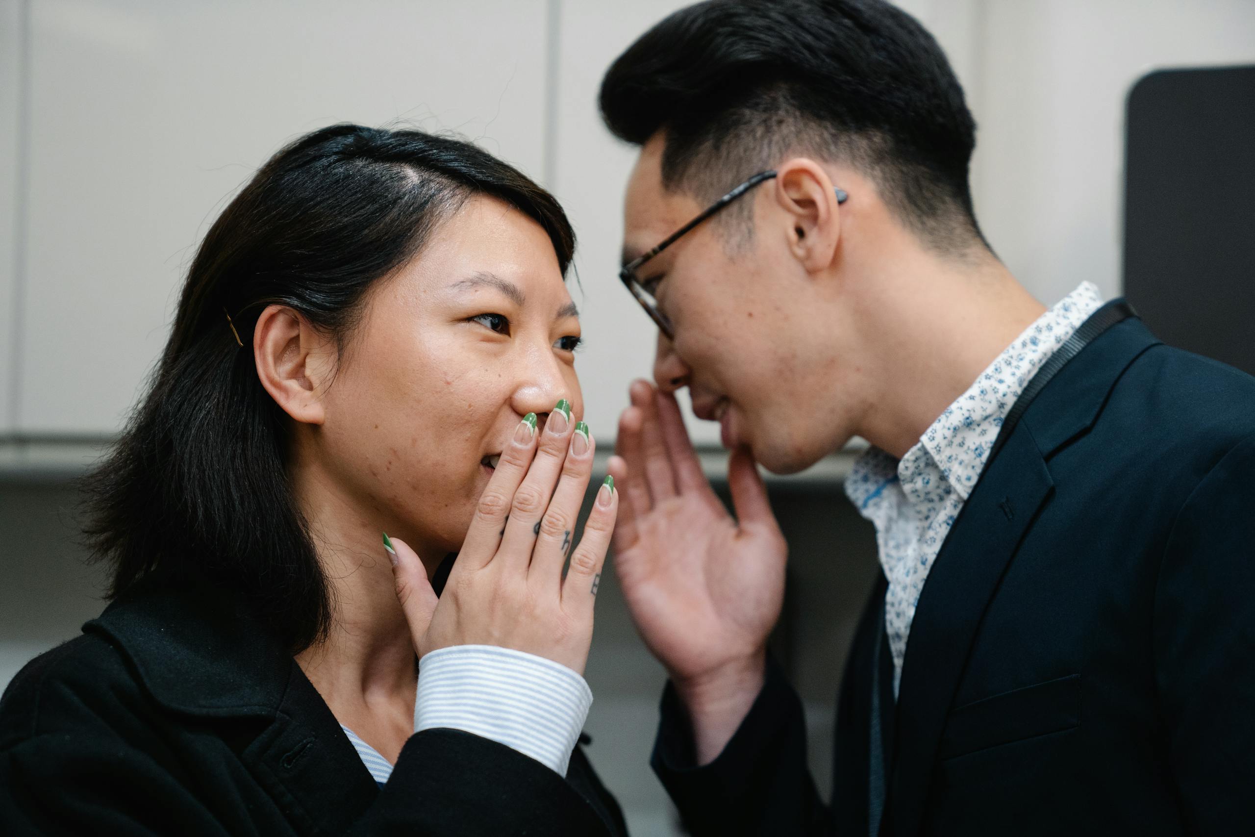 Close-up of an Asian man and woman whispering secrets while indoors.