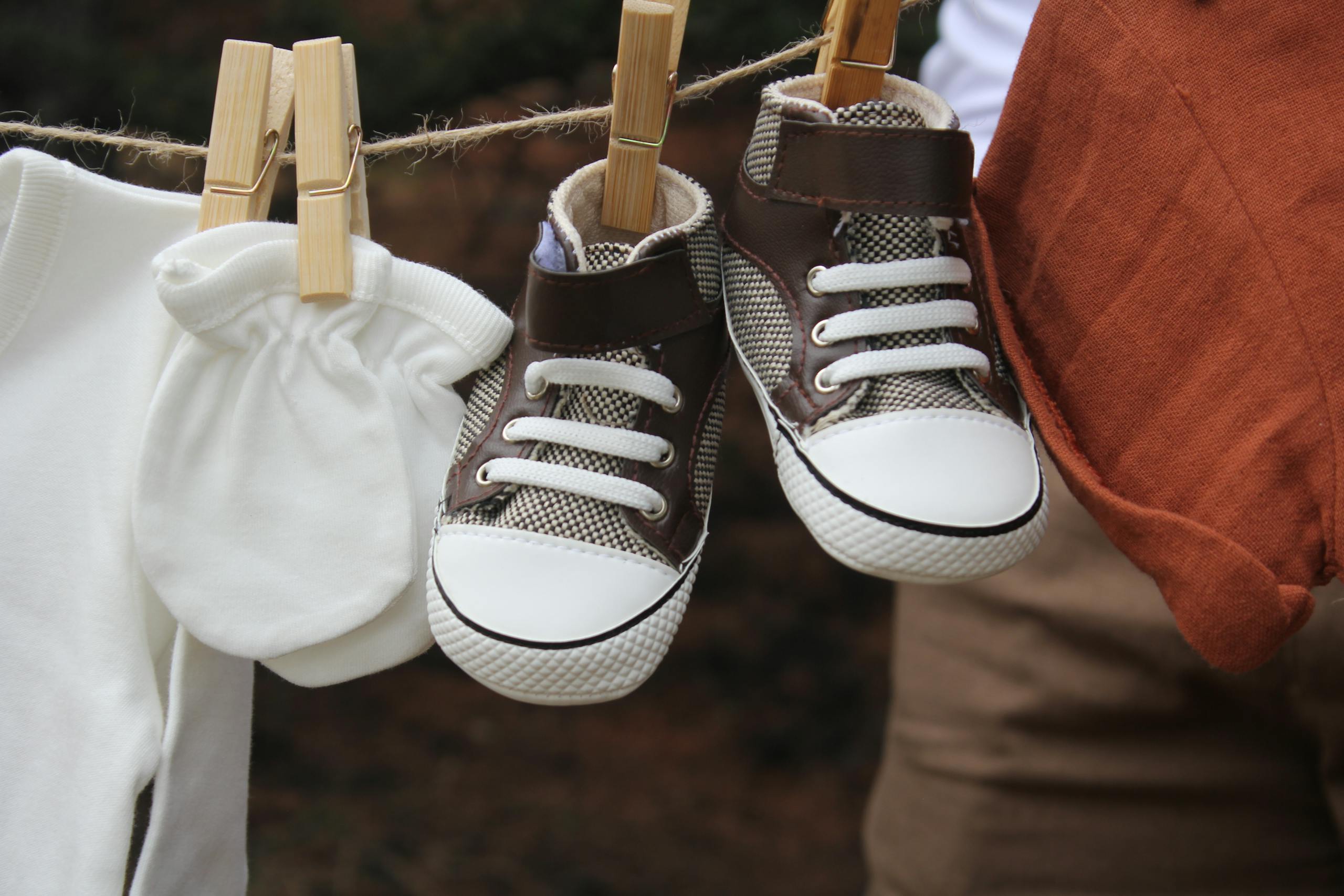 Close-up of baby shoes and clothing drying outdoors on a clothesline.