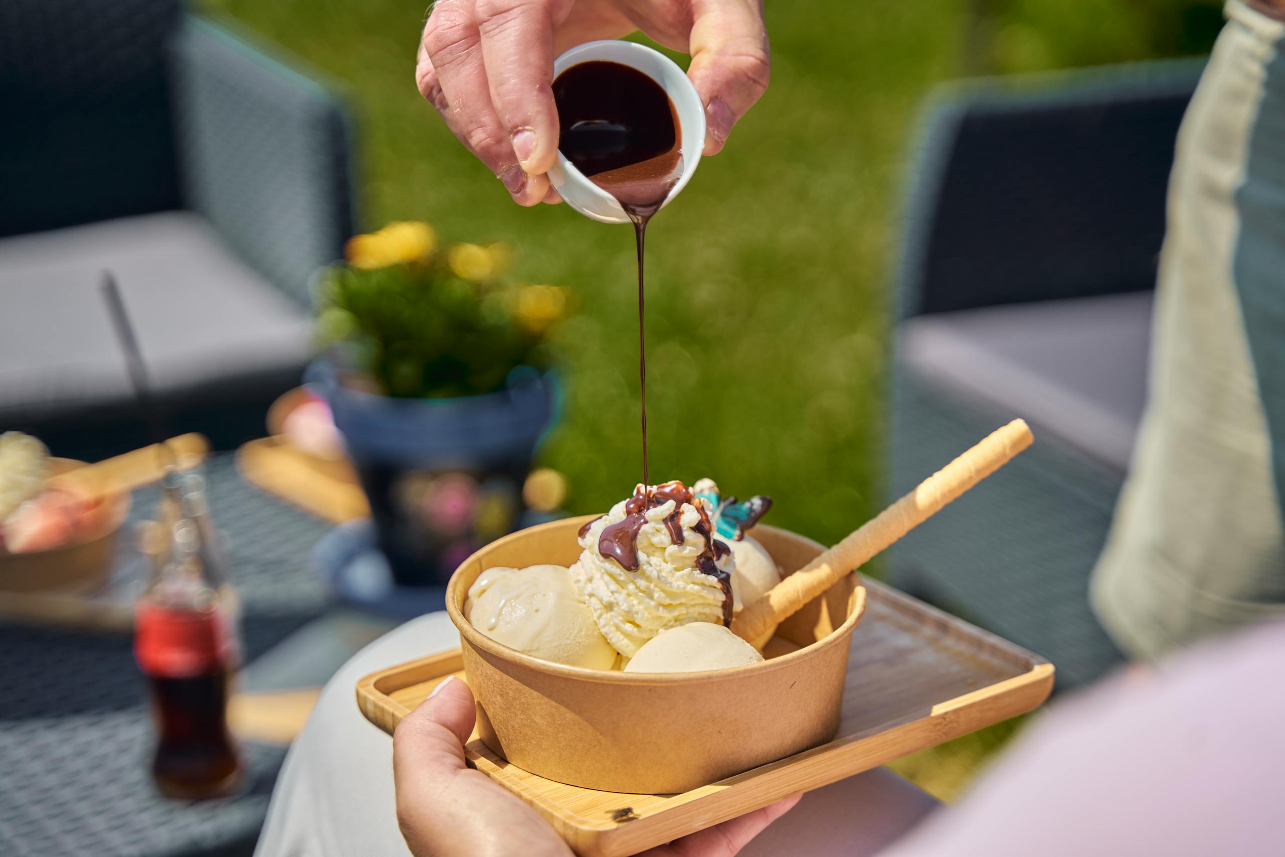 Close-up of chocolate sauce being poured over a bowl of vanilla ice cream outdoors.