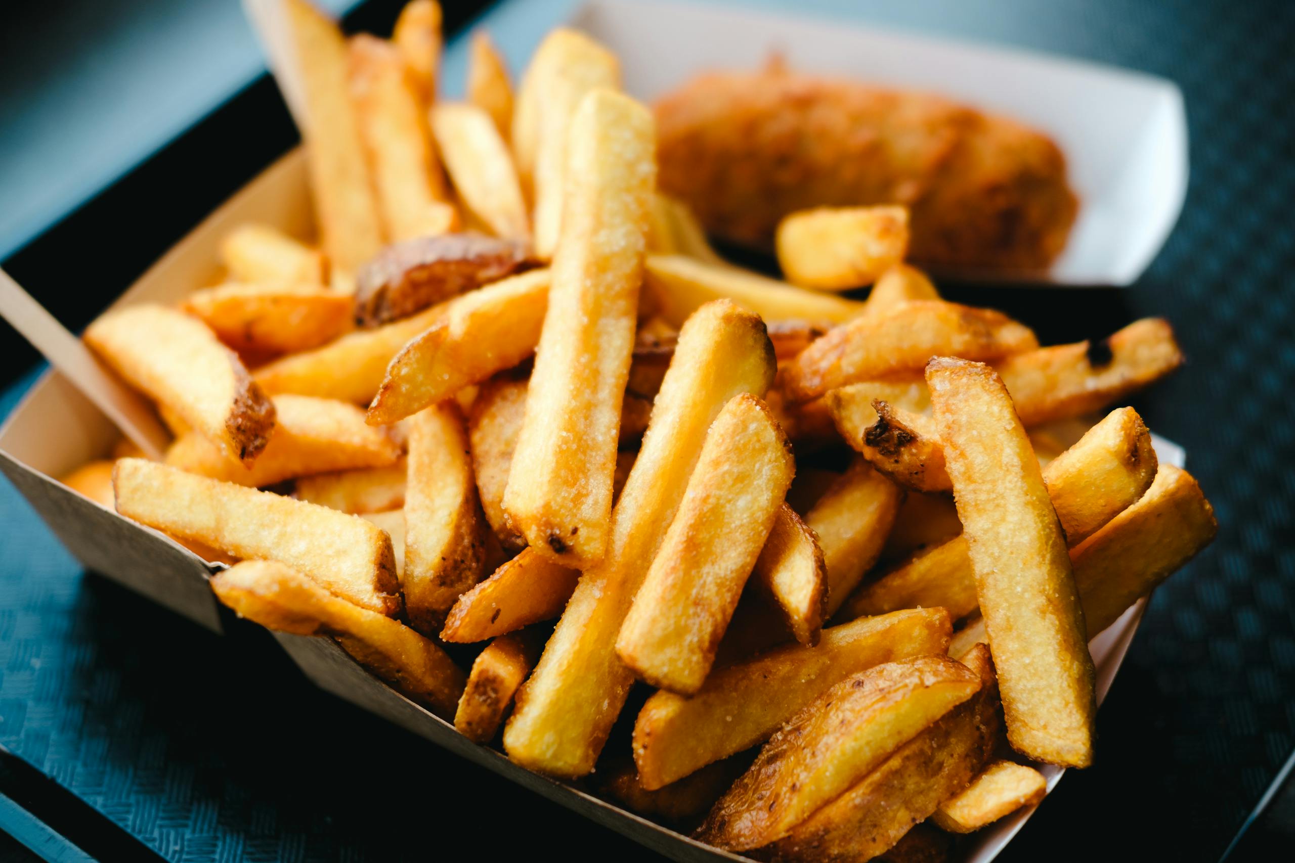 Close-up of delicious golden French fries in a paper box, served as a perfect snack or side dish.