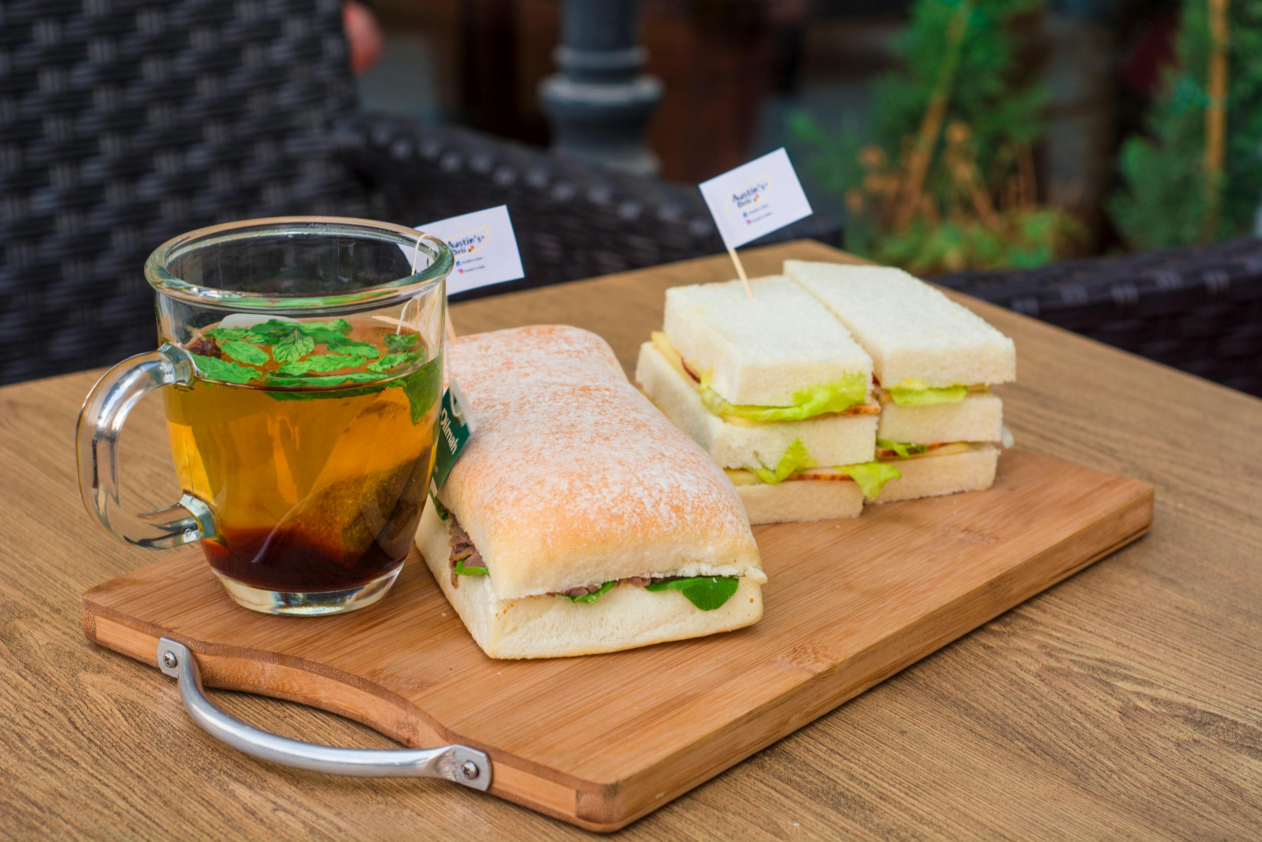 Close-up of freshly made sandwiches and herbal mint tea on a wooden tray, perfect for a cozy meal.