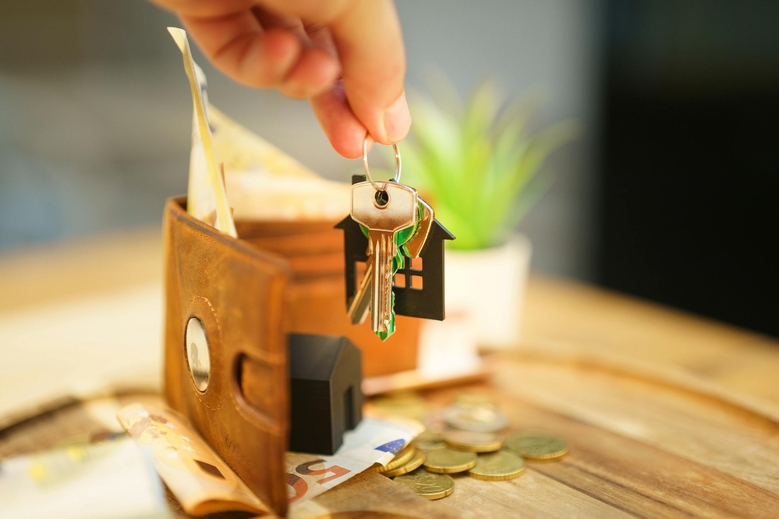 Close-up of hand holding a house key with a wallet and coins, symbolizing real estate investment.
