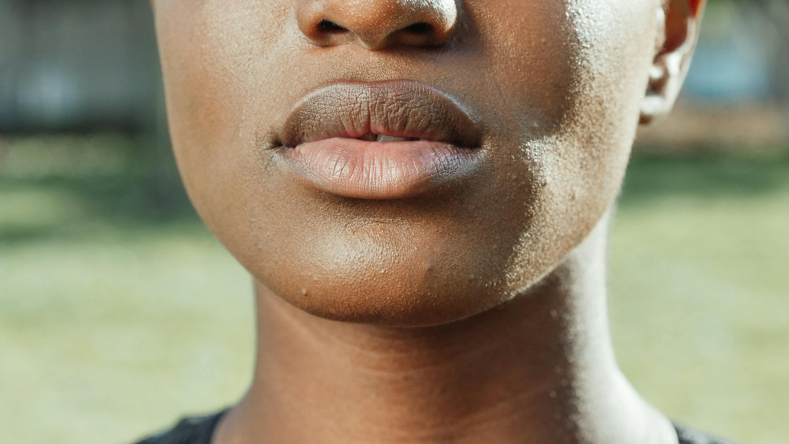 Close-up of lips and skin in natural light, showcasing texture and complexion outdoors.