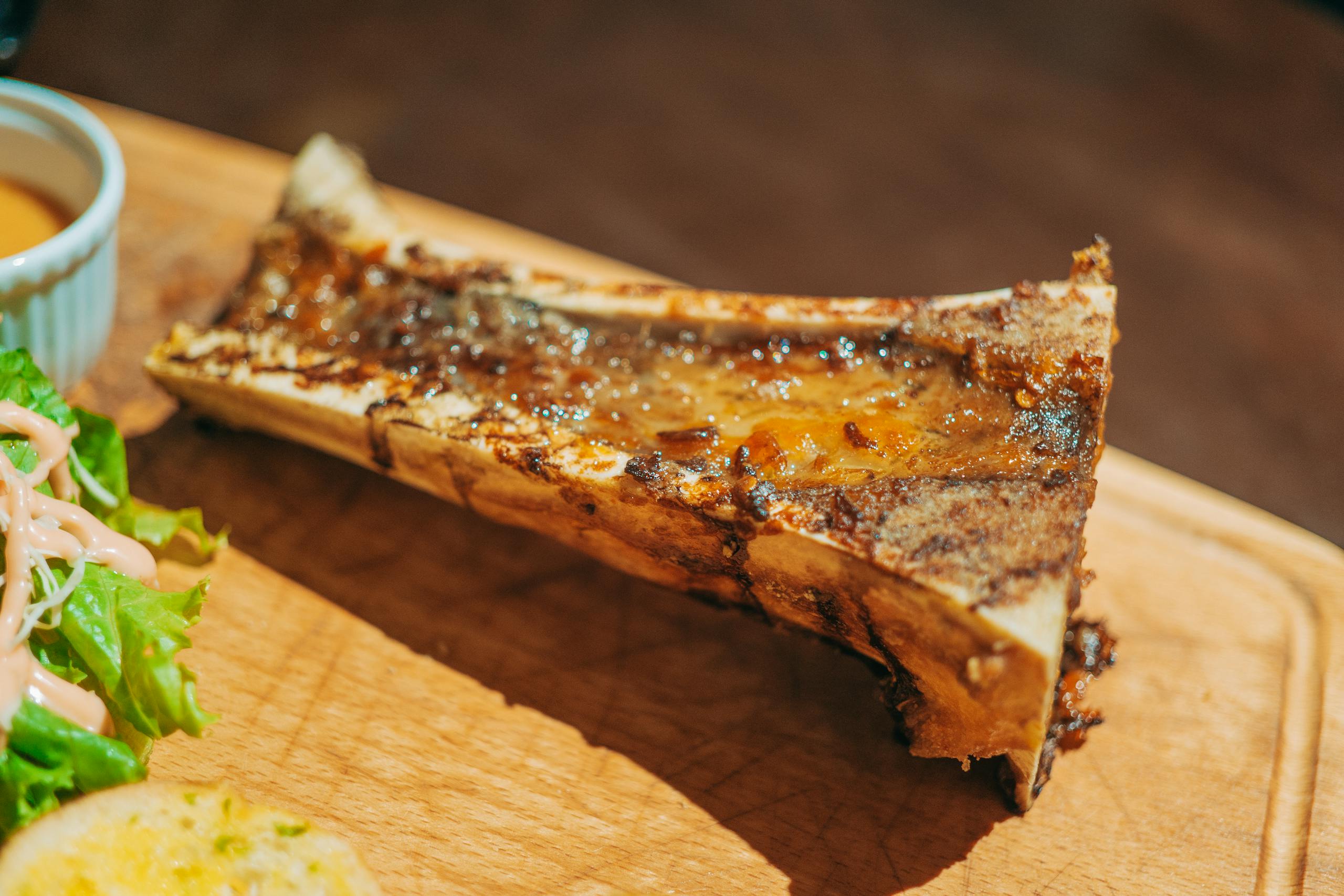 Close-up of roasted bone marrow served on a wooden board with salad and sauce.