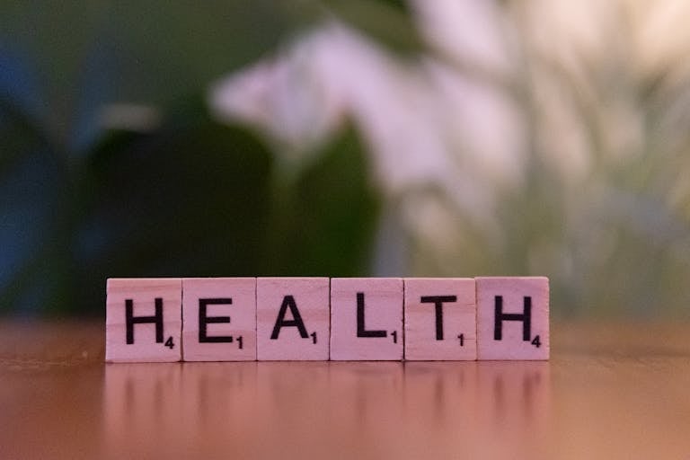 Close-up of Scrabble tiles spelling 'Health' on a wooden table with a blurred background.