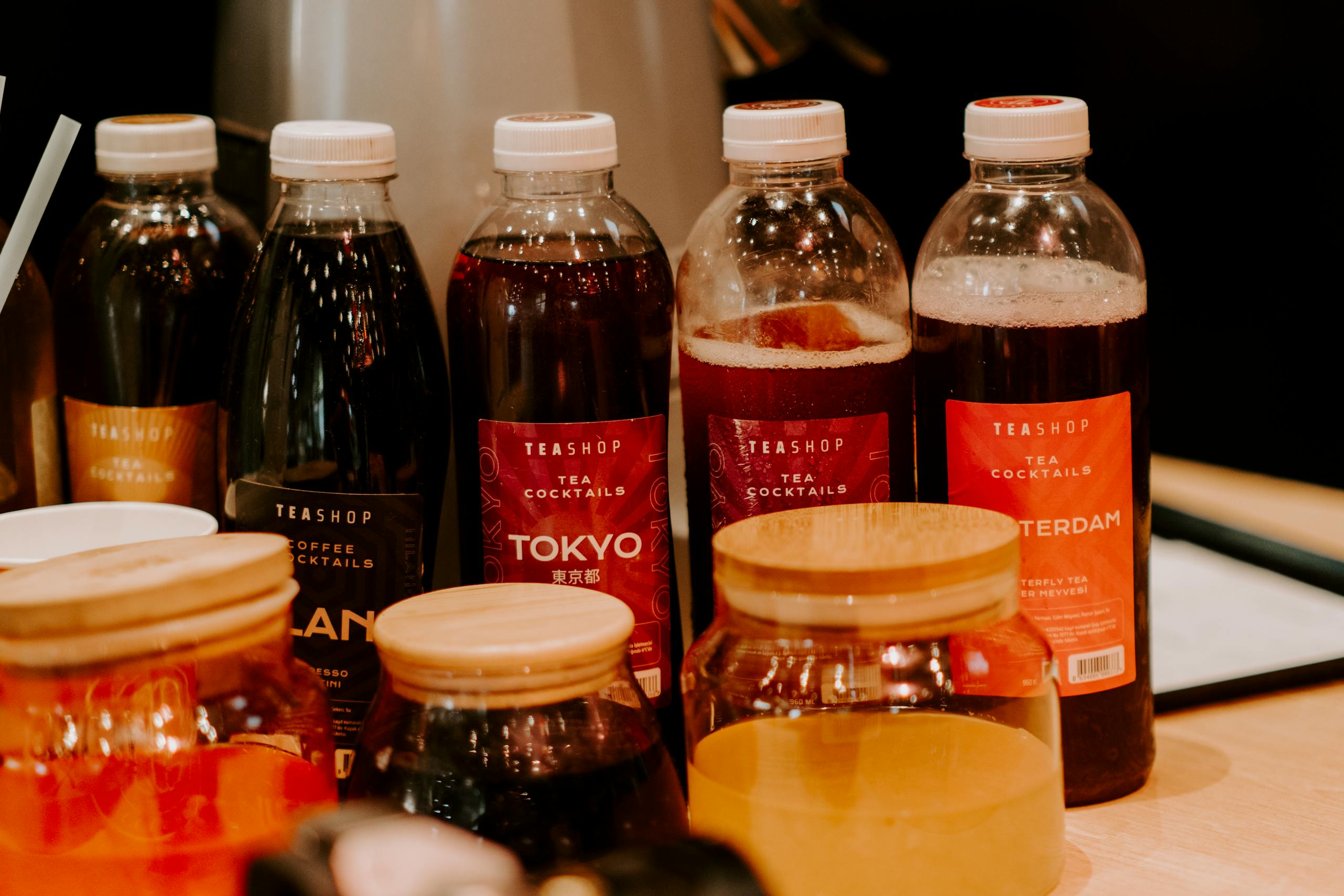 Close-up of various bottled tea cocktails with labels in a cozy setting.