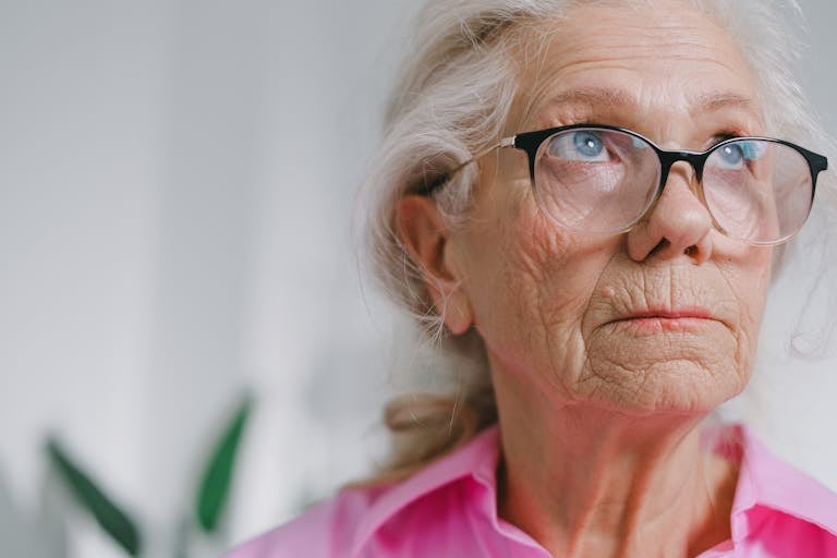 Close-up portrait of a thoughtful elderly woman wearing glasses indoors.