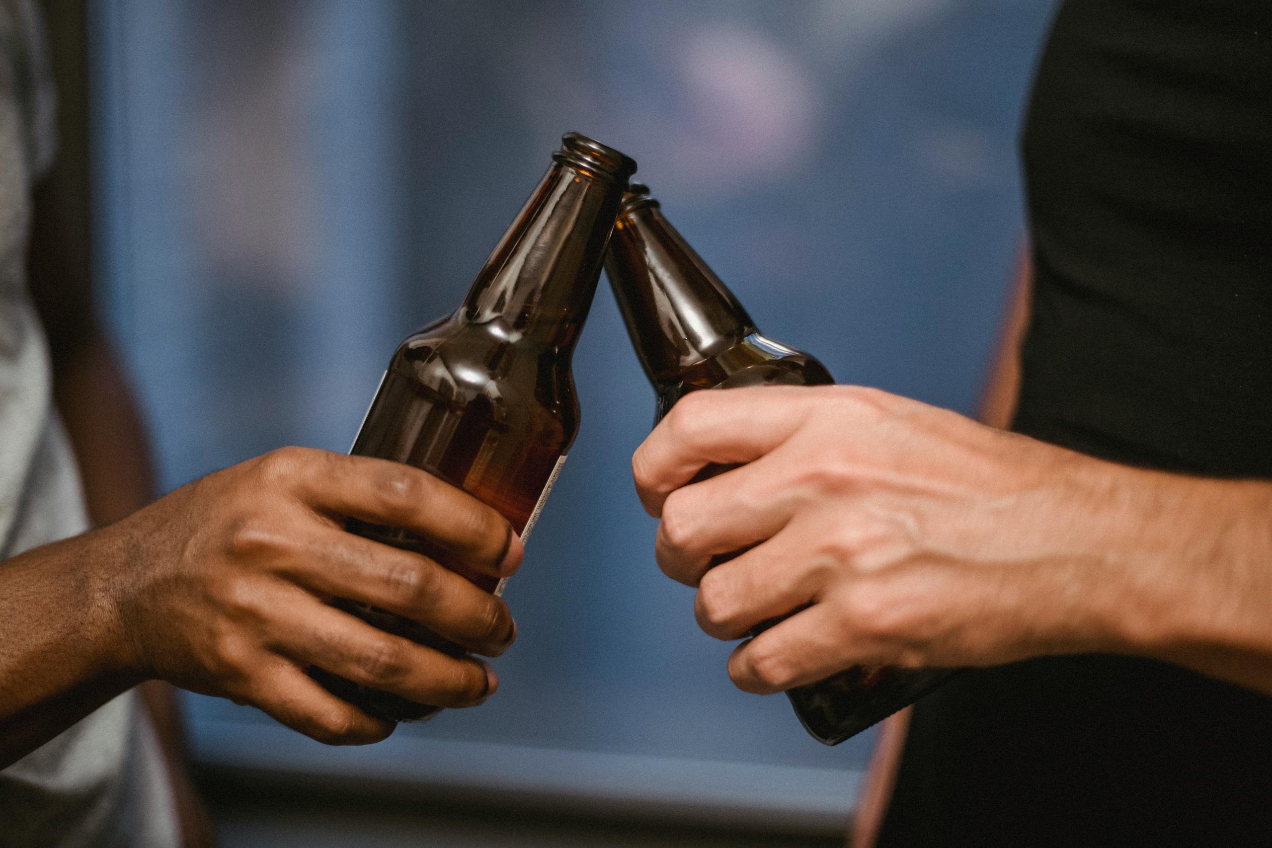 Close-up shot of two individuals clinking beer bottles in a casual indoor setting.
