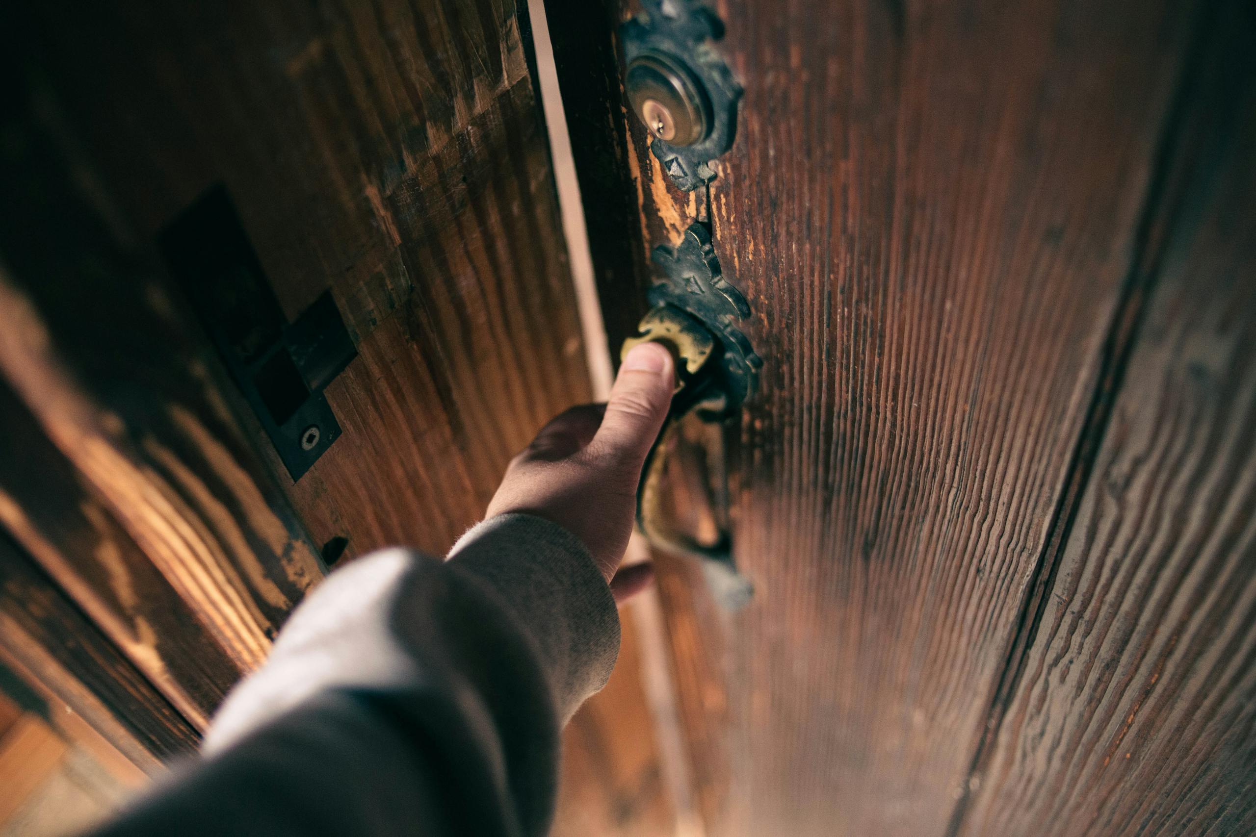 Close-up view of a hand opening a vintage wooden door with ornate handle, creating a warm and inviting atmosphere.
