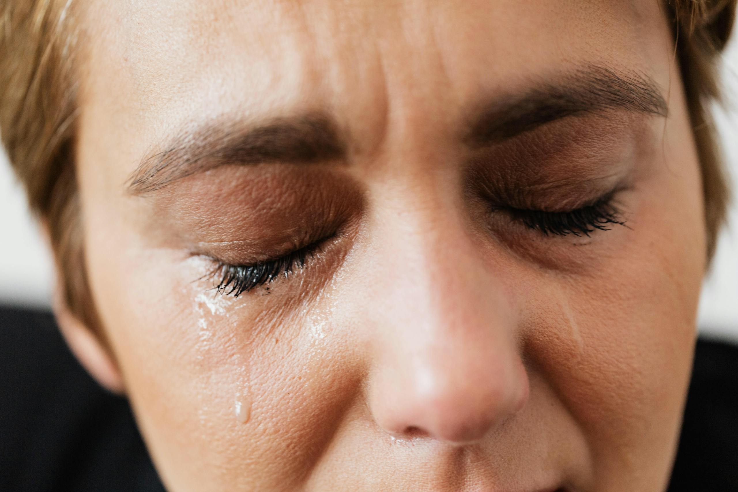 Closeup of crop unrecognizable middle aged woman suffering from depression and crying with closed eyes