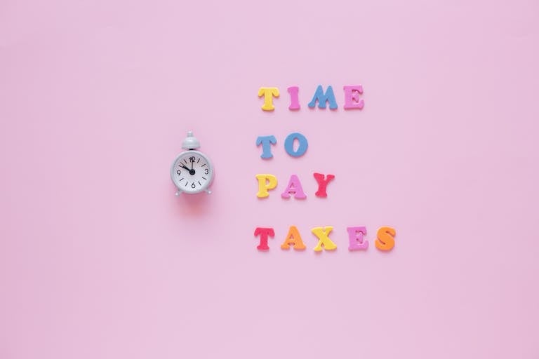 Colorful letters spell 'Time to Pay Taxes' next to a clock on a pink surface.