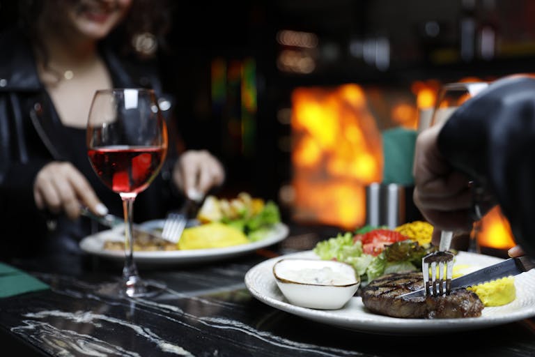 Couple enjoying a cozy dinner with steak and red wine in a warm, intimate setting.