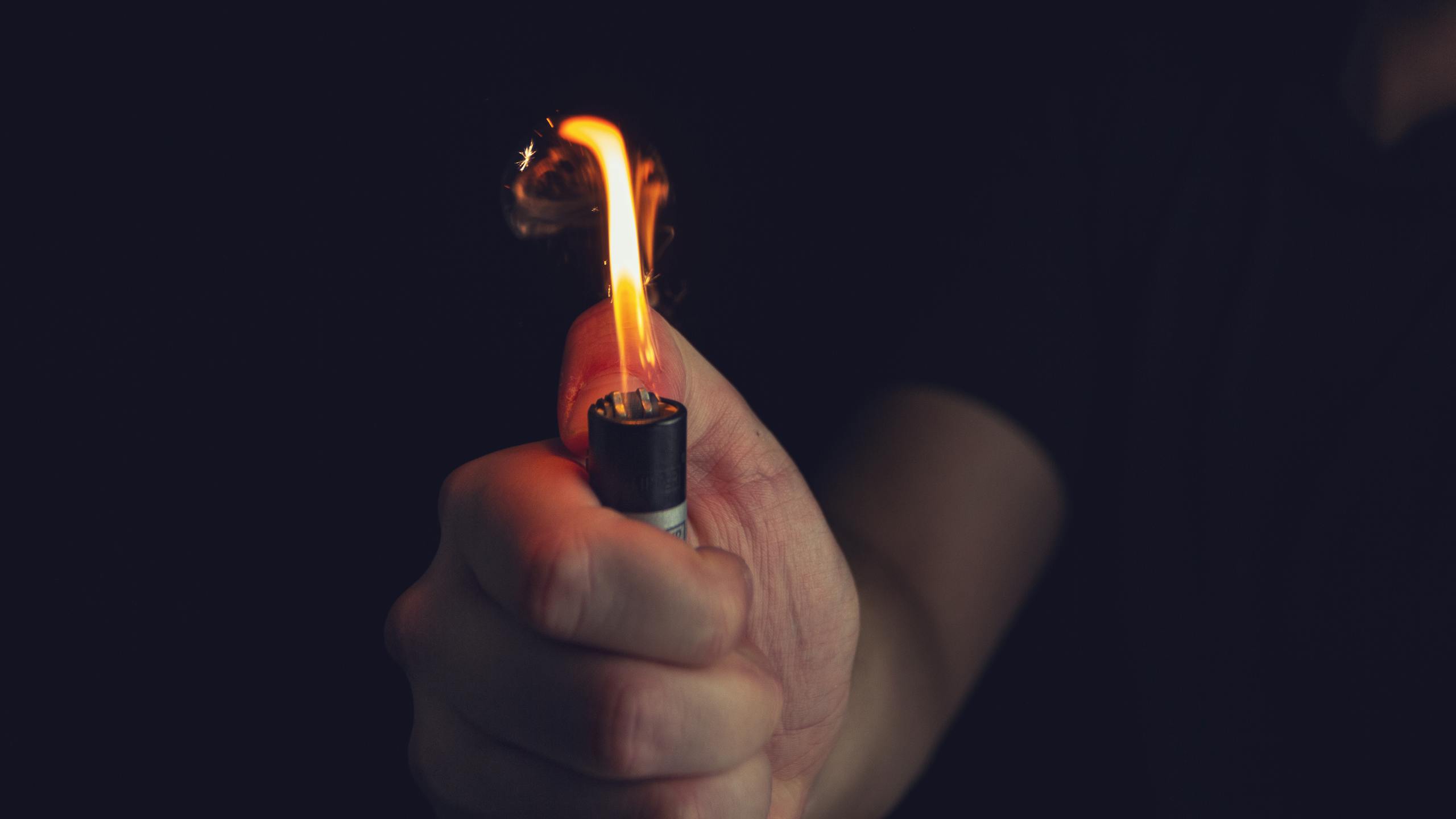 Crop anonymous male in black shirt holding bright burning lighter in dark room