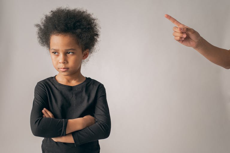 Crop anonymous person pointing up with index finger while scolding unhappy African American girl looking away while standing on white background in studio