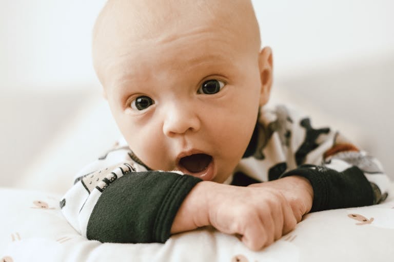 Cute newborn baby in patterned outfit showing an adorable and curious expression while lying indoors.