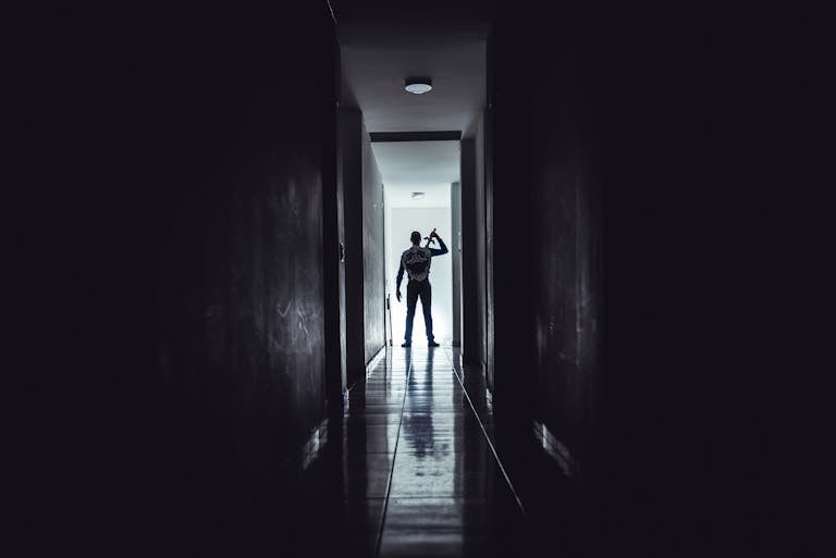Dark, dramatic silhouette of a man holding a sword in a narrow hallway, creating an intense atmosphere.