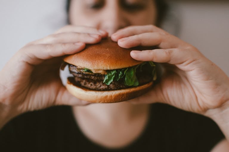 Delicious beef burger with fresh lettuce held by a woman's hands, focus on the food.