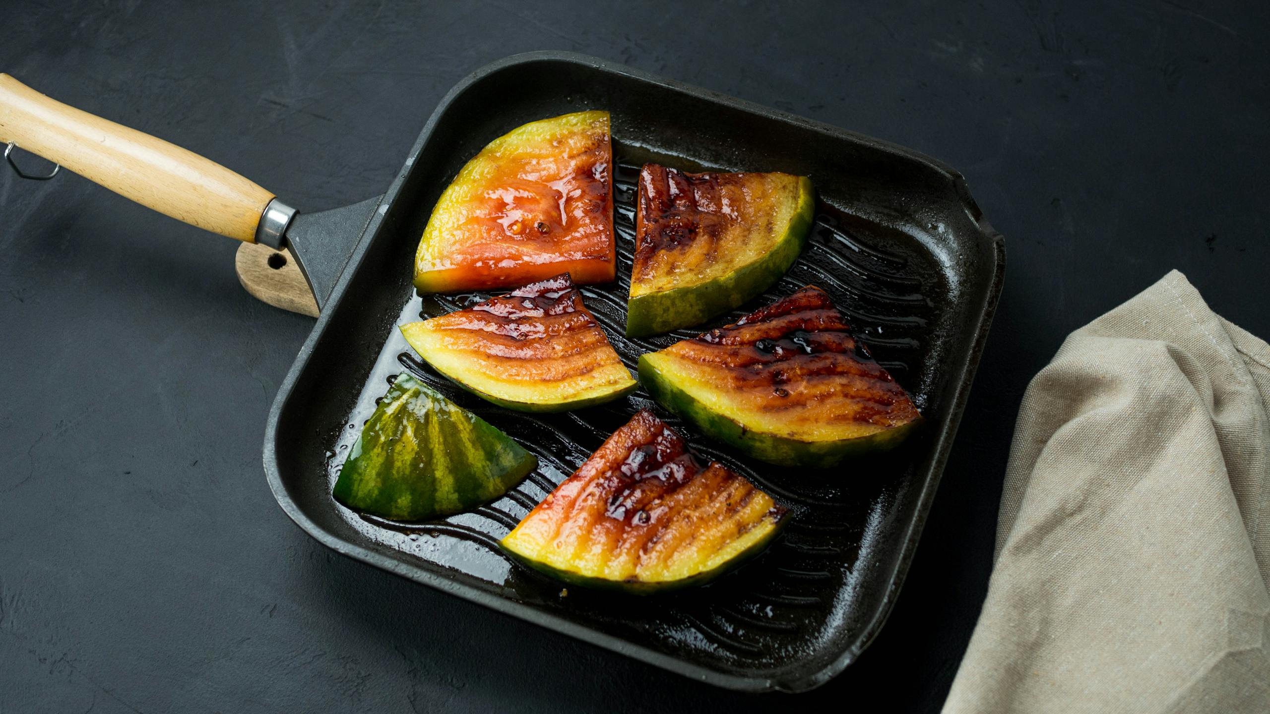 Delicious grilled watermelon slices on a black frying pan, perfect for a summer dish.