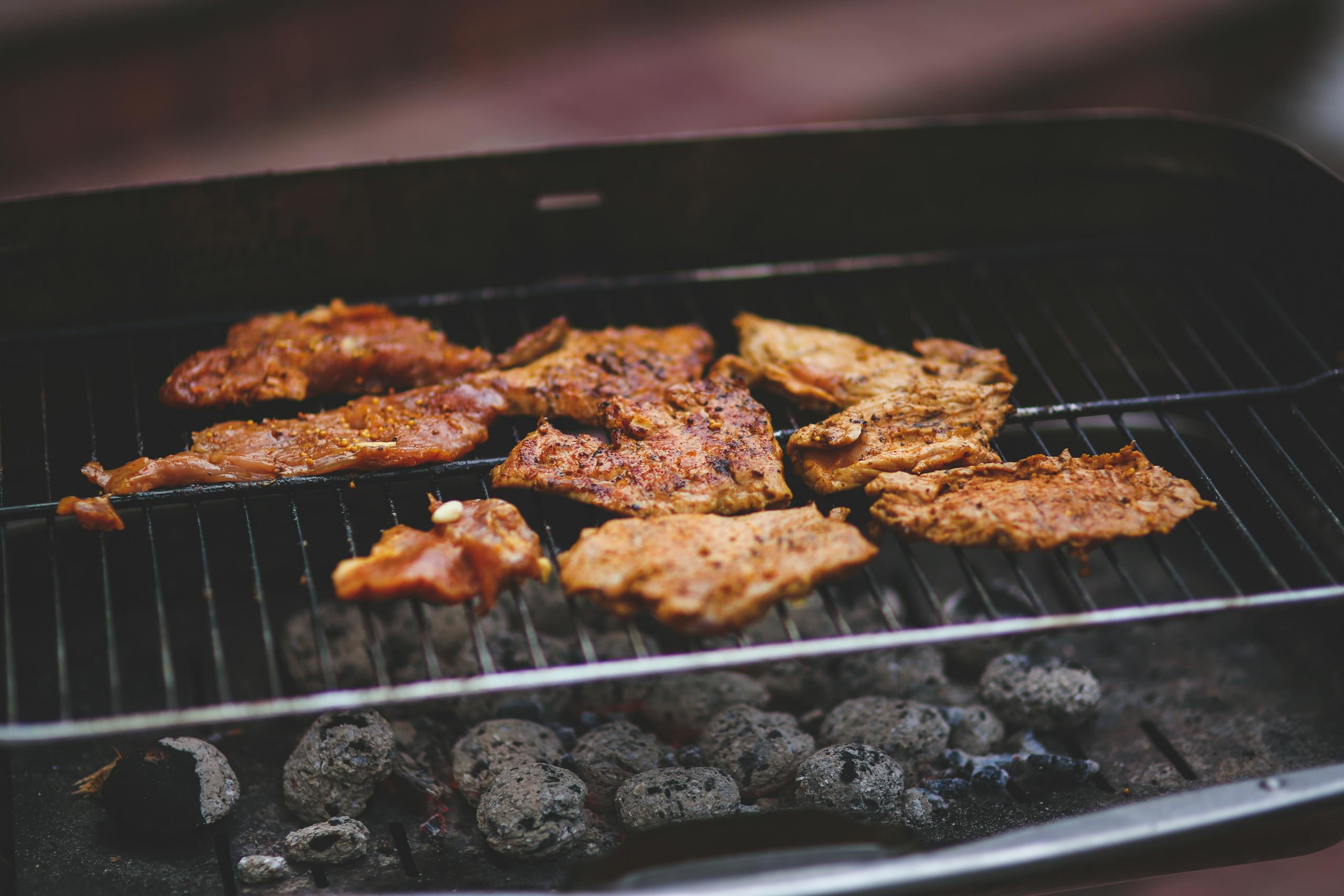 Delicious marinated meats sizzling on a charcoal barbecue grill, perfect for outdoor summer cooking.