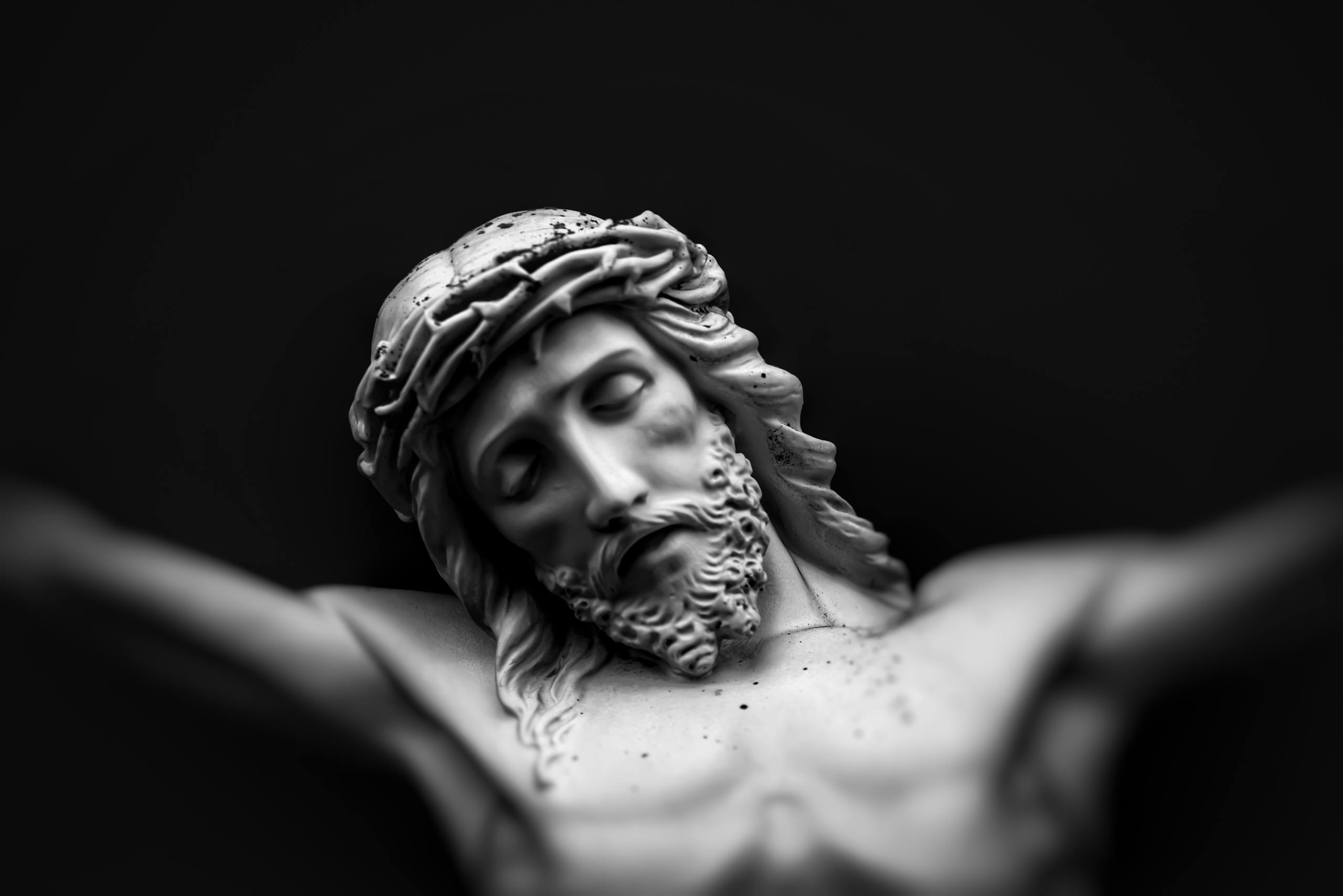 Detailed black and white close-up of a Jesus statue with a crown of thorns, conveying a solemn and spiritual mood.