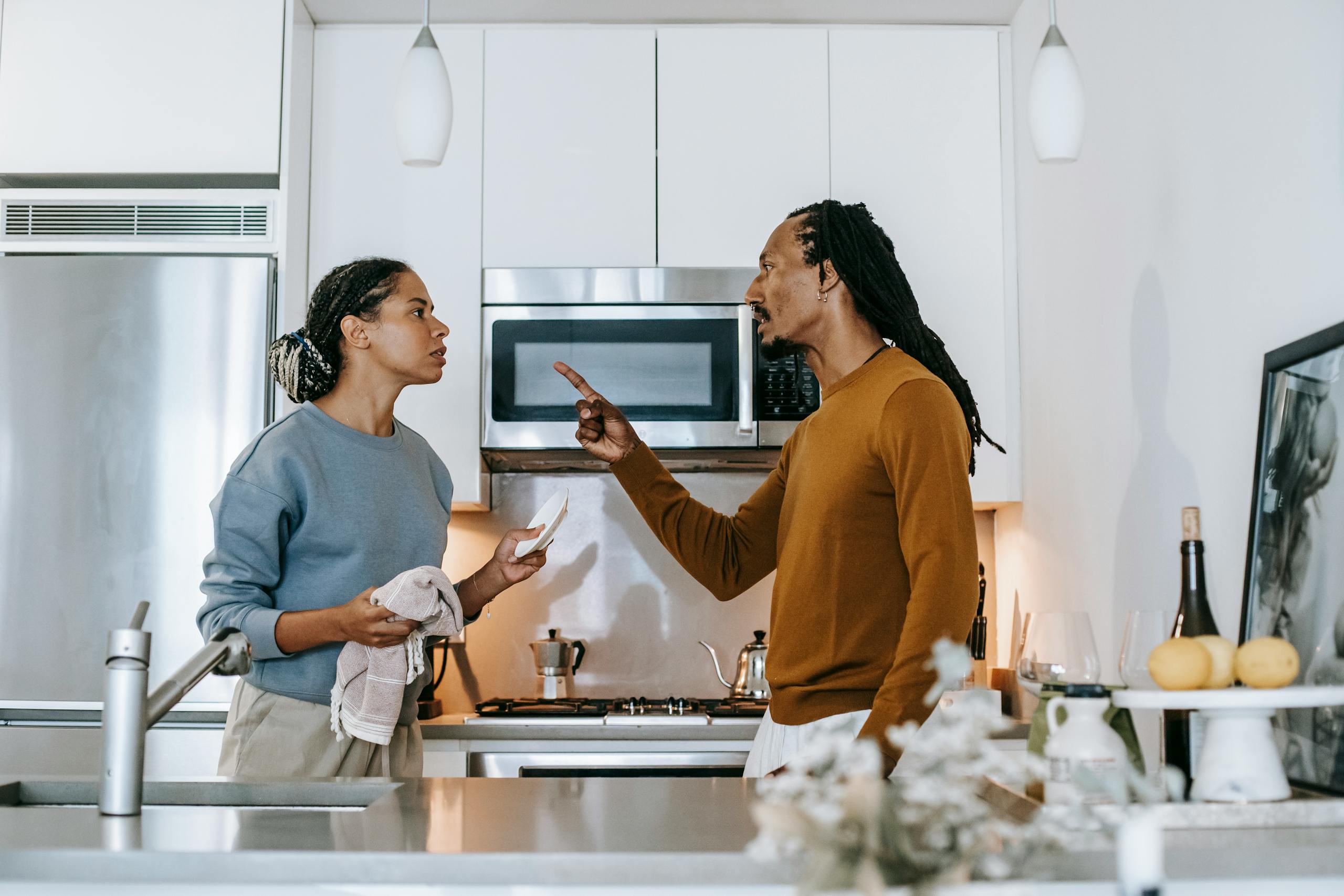 A discontented African American male menacing to female partner with finger up while looking at each other during dispute at home
