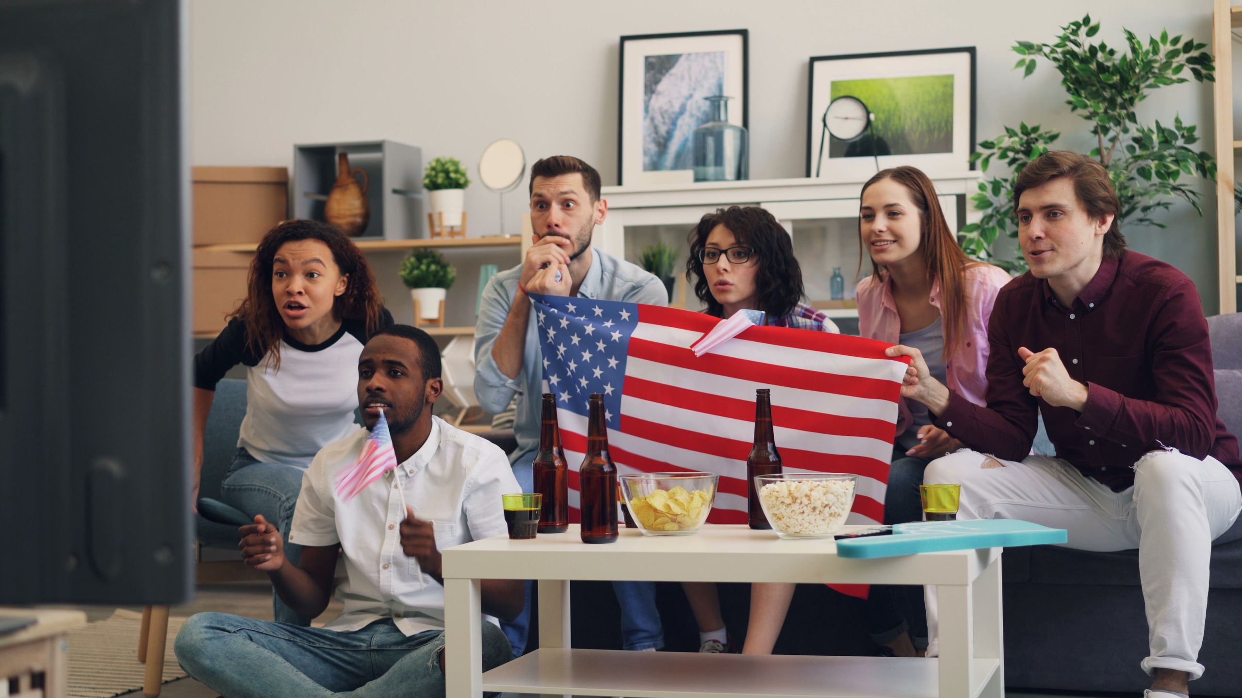 Diverse group of friends enjoying a sports event at home, holding an American flag.