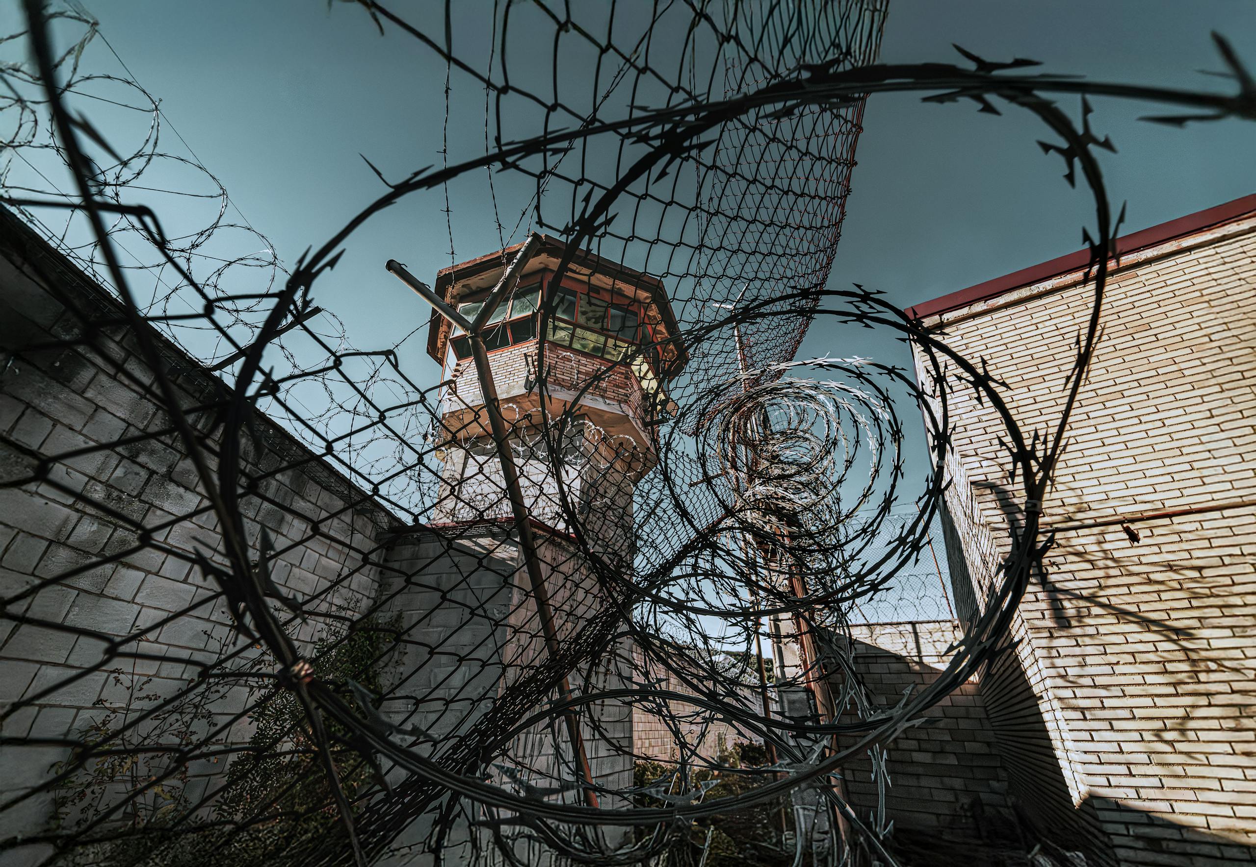 Dramatic view of a guard tower through barbed wire in a prison yard, symbolizing security and confinement.