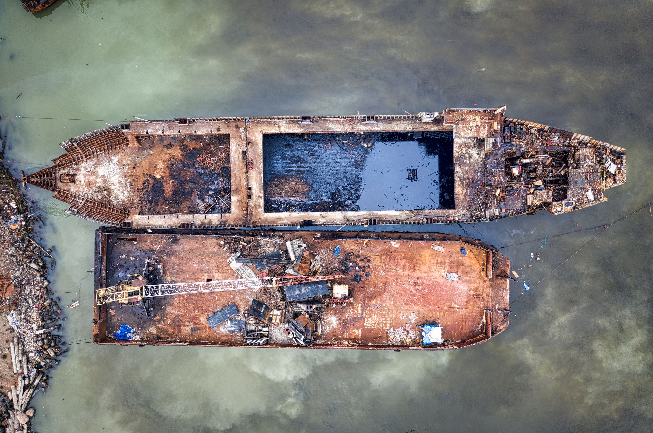 Drone view of aged abandoned ships covered with rust moored in polluted water of sea in daytime