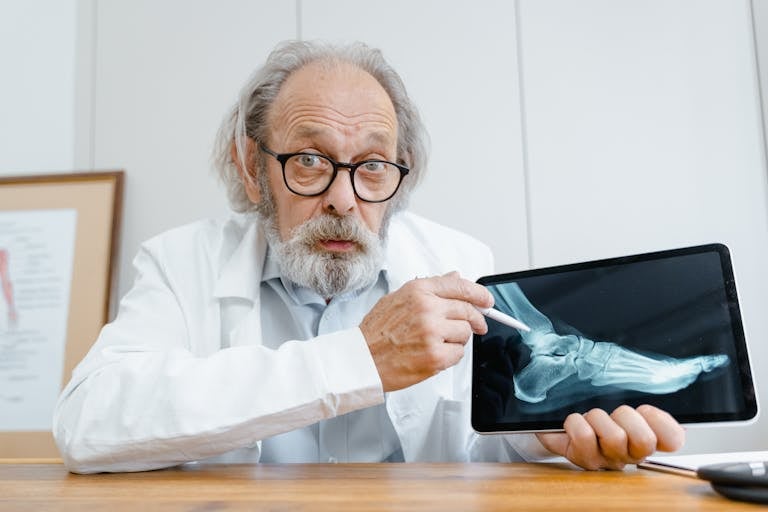 Elderly doctor examining an X-ray on a digital tablet in a clinical setting.