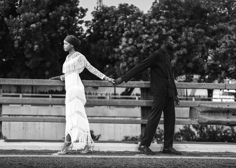 Elegant black and white image of a couple holding hands on a bridge, showcasing contrast and emotion.