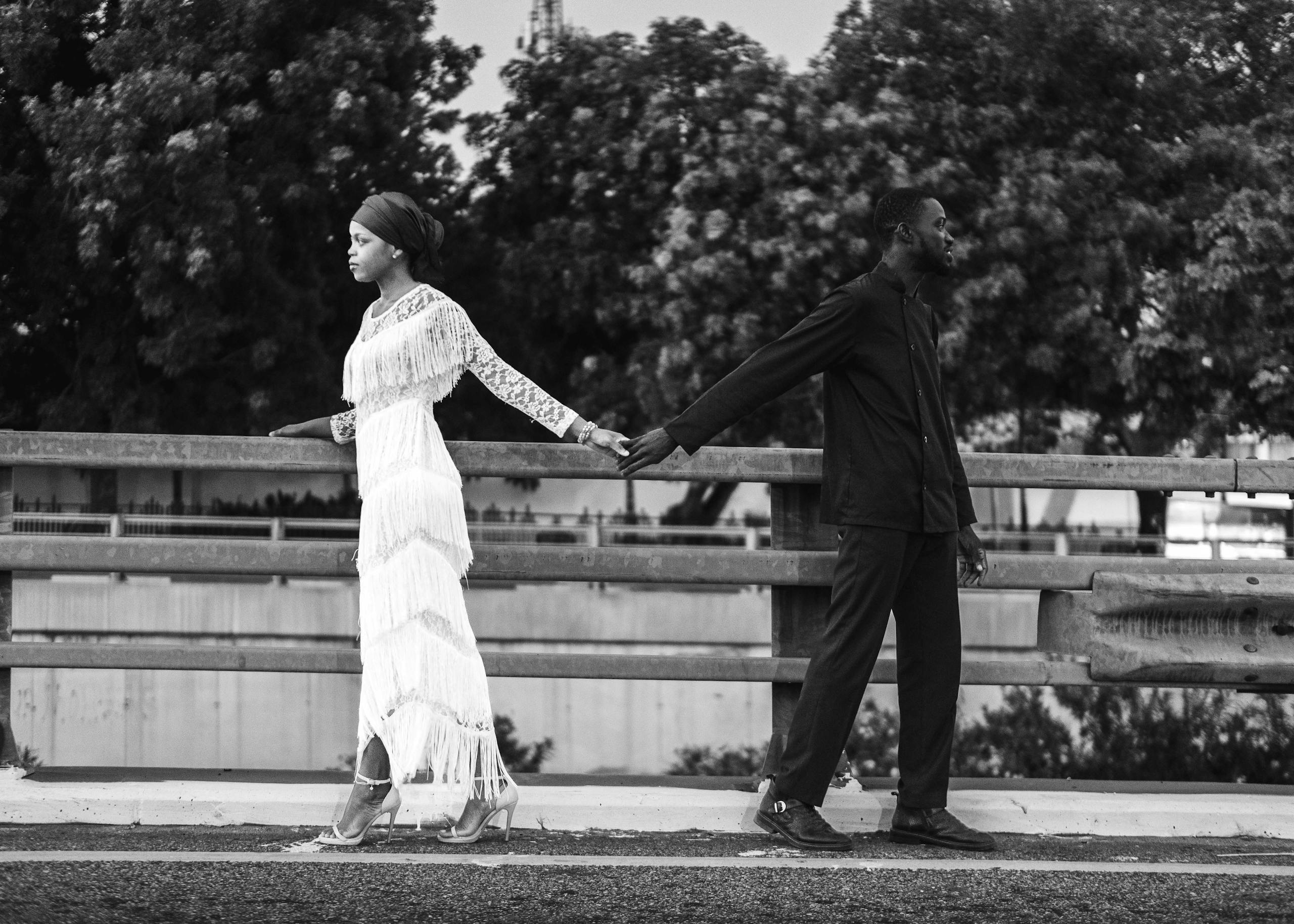 Elegant black and white image of a couple holding hands on a bridge, showcasing contrast and emotion.