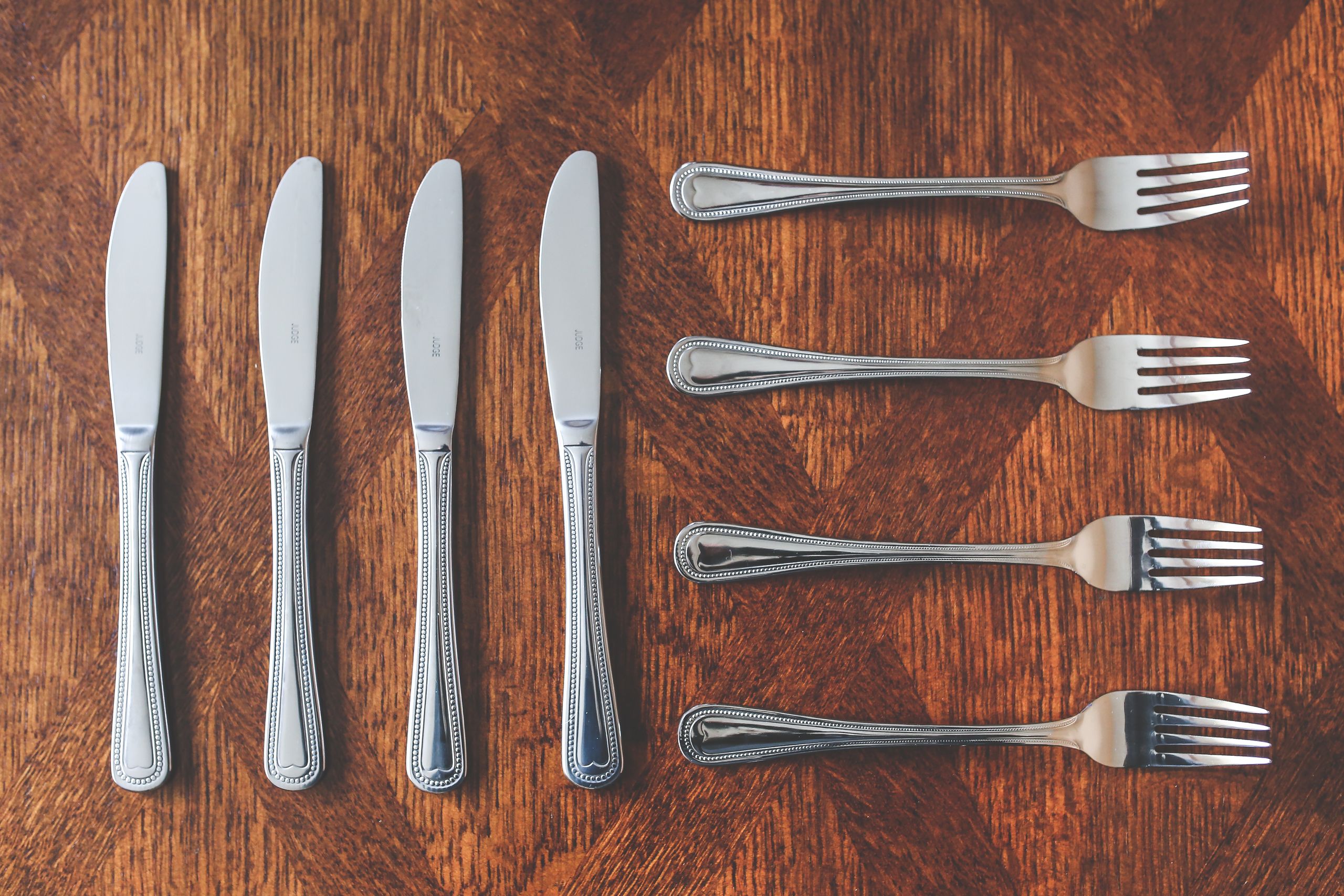 Elegant silver knives and forks arranged on a textured wooden table.