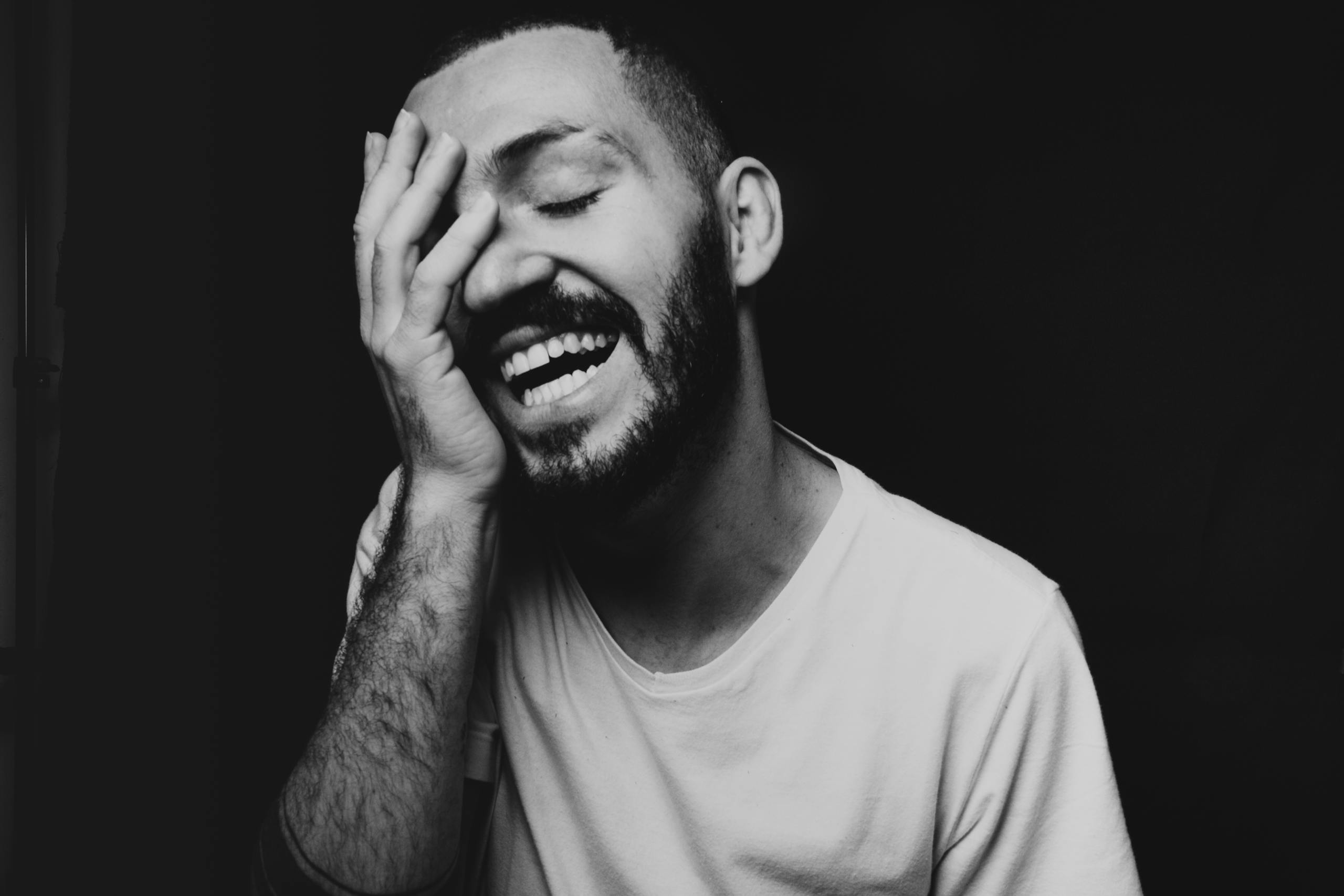 Emotional black and white portrait of a young man smiling with hand on face.