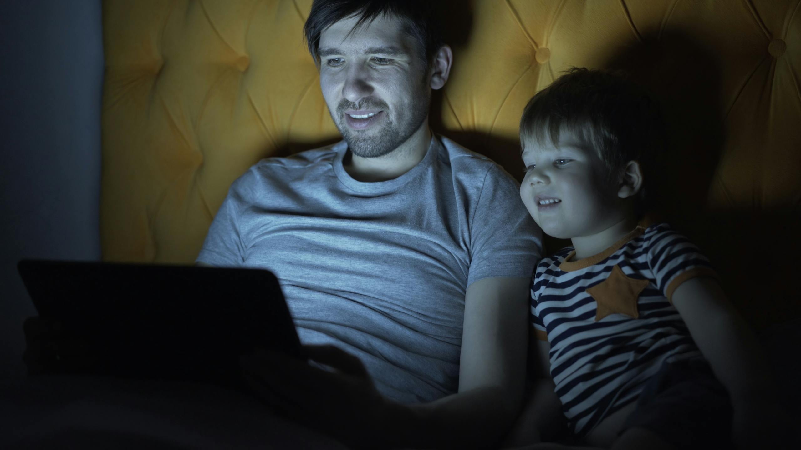 Father and son bonding, watching tablet in dim light, evening routine.