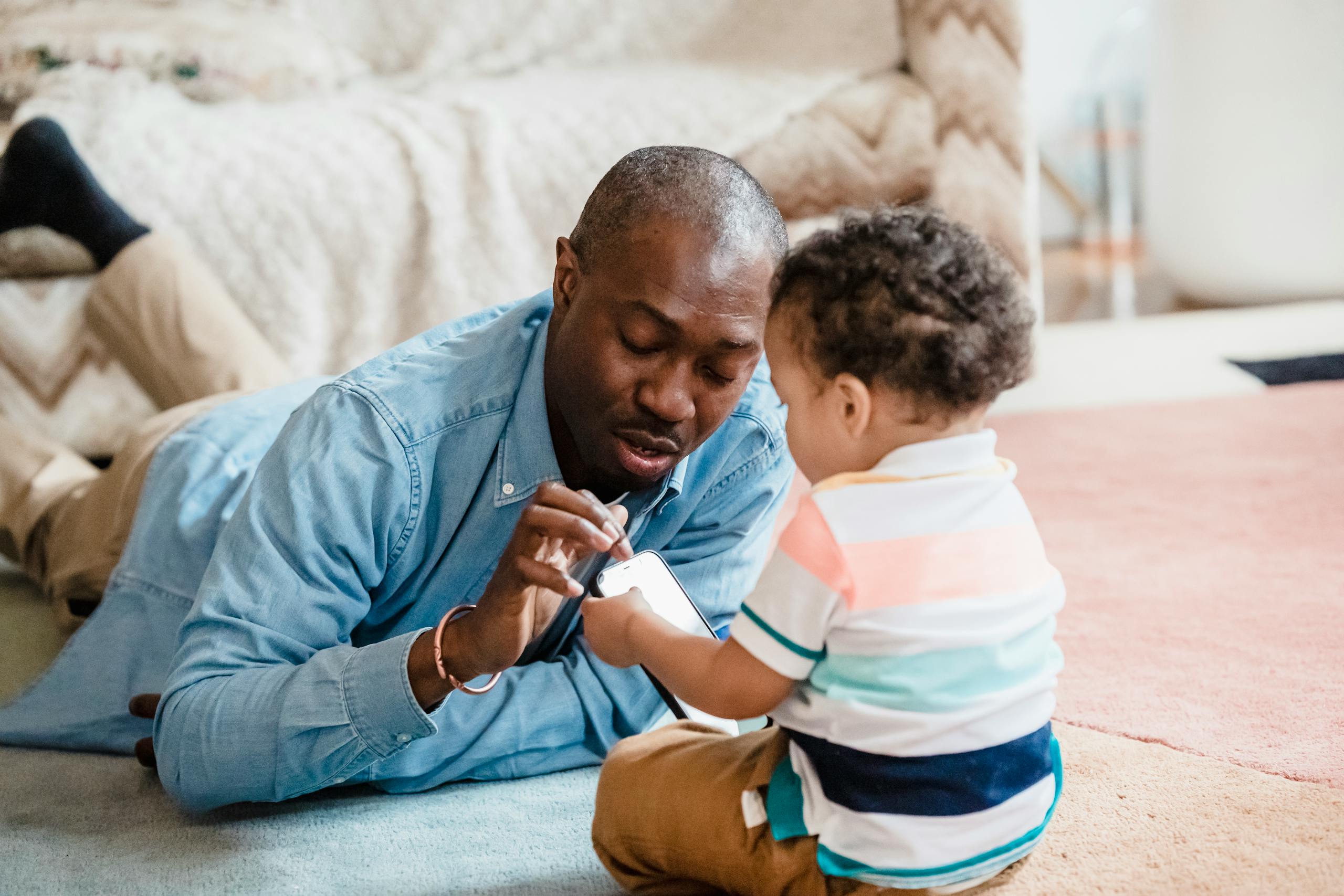 Father and toddler engaging with smartphone, building family bond in cozy home setting.