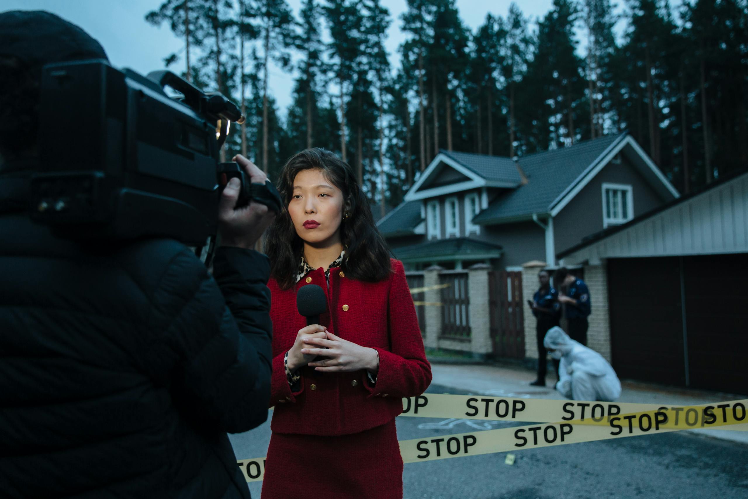 Female journalist reporting live from a crime scene with police and cameraman.