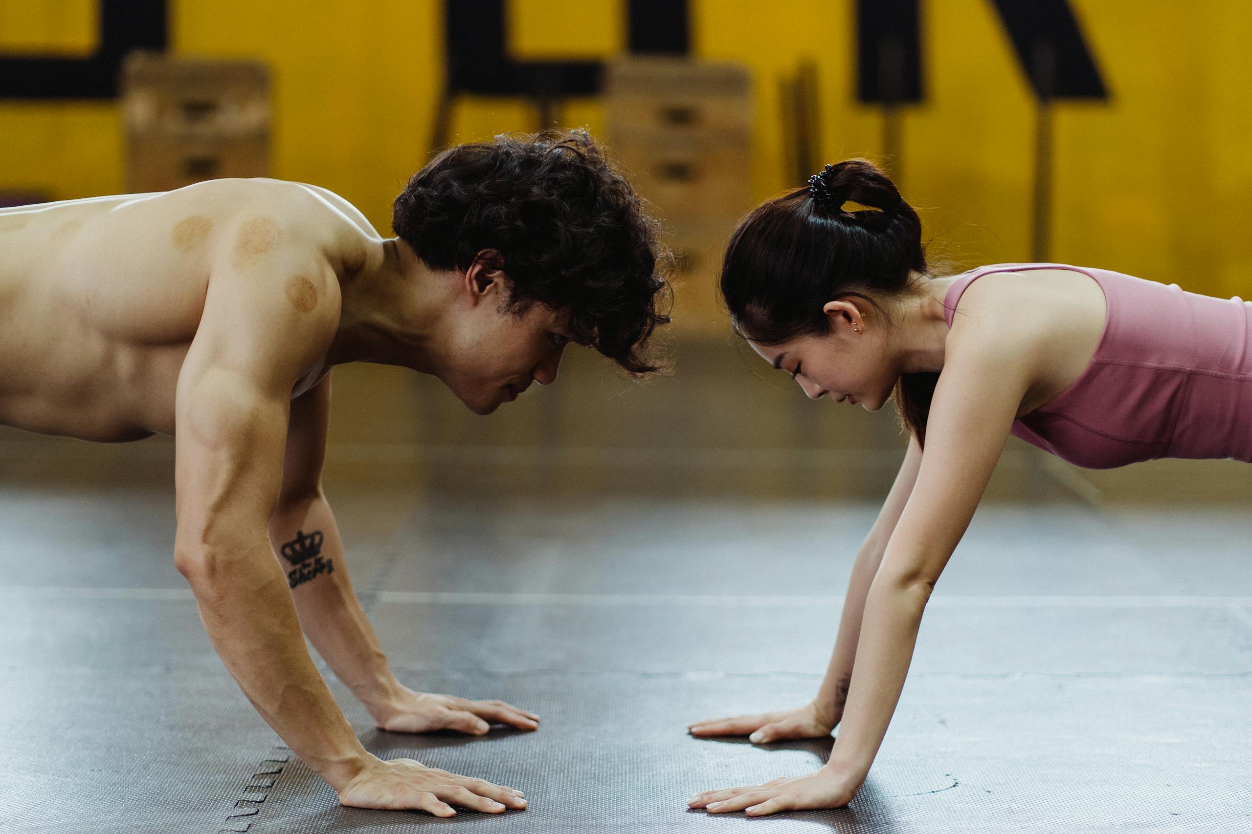 Fit Asian man and woman doing push-ups face to face in a gym setting, promoting fitness and health.