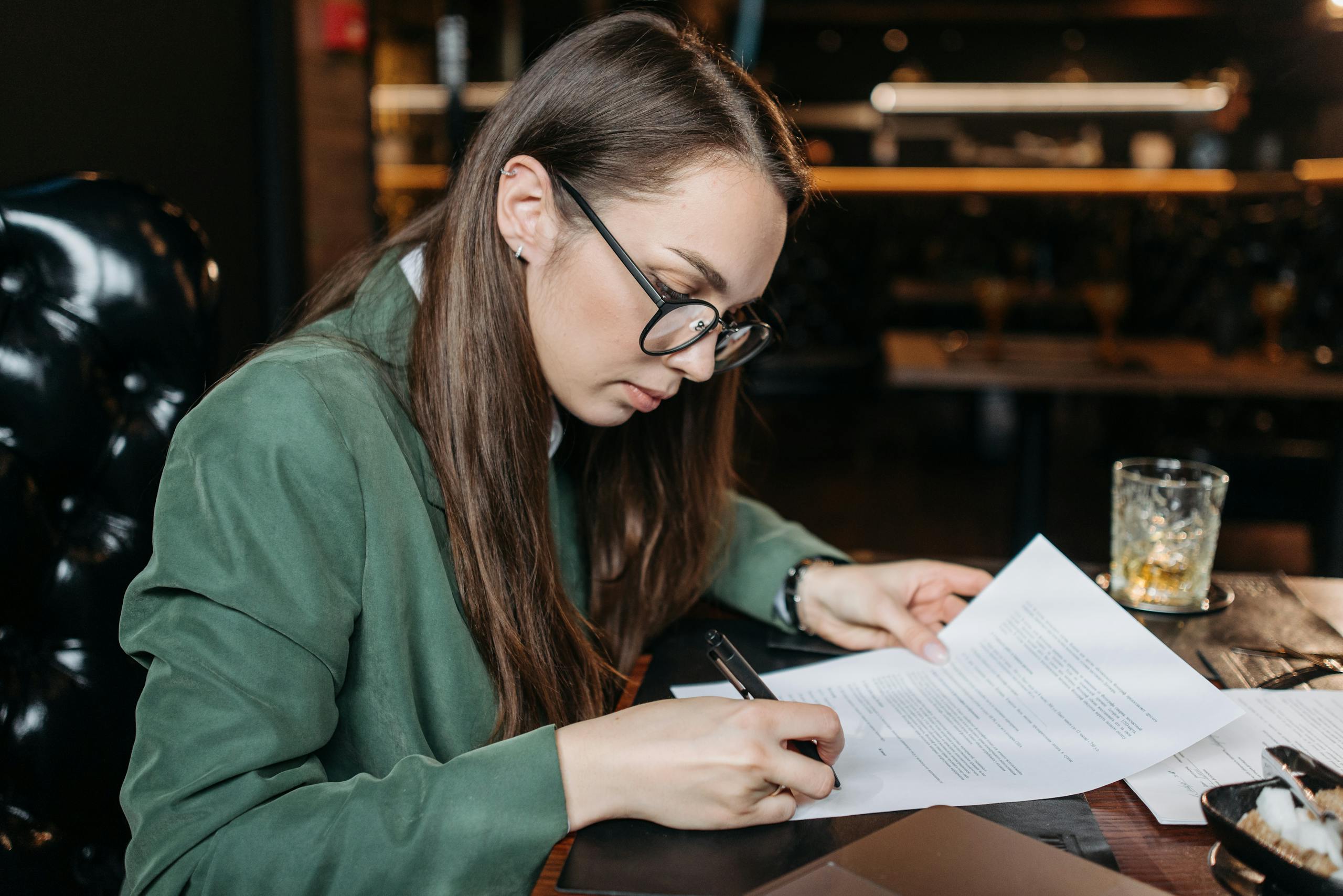 Focused businesswoman in green attire signing important documents at her desk.