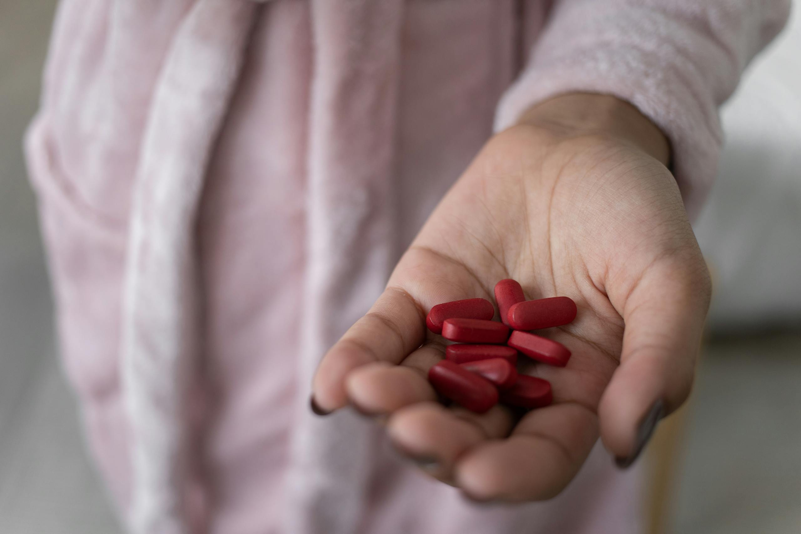 Focused image of a hand holding red pills, symbolizing health and medication.