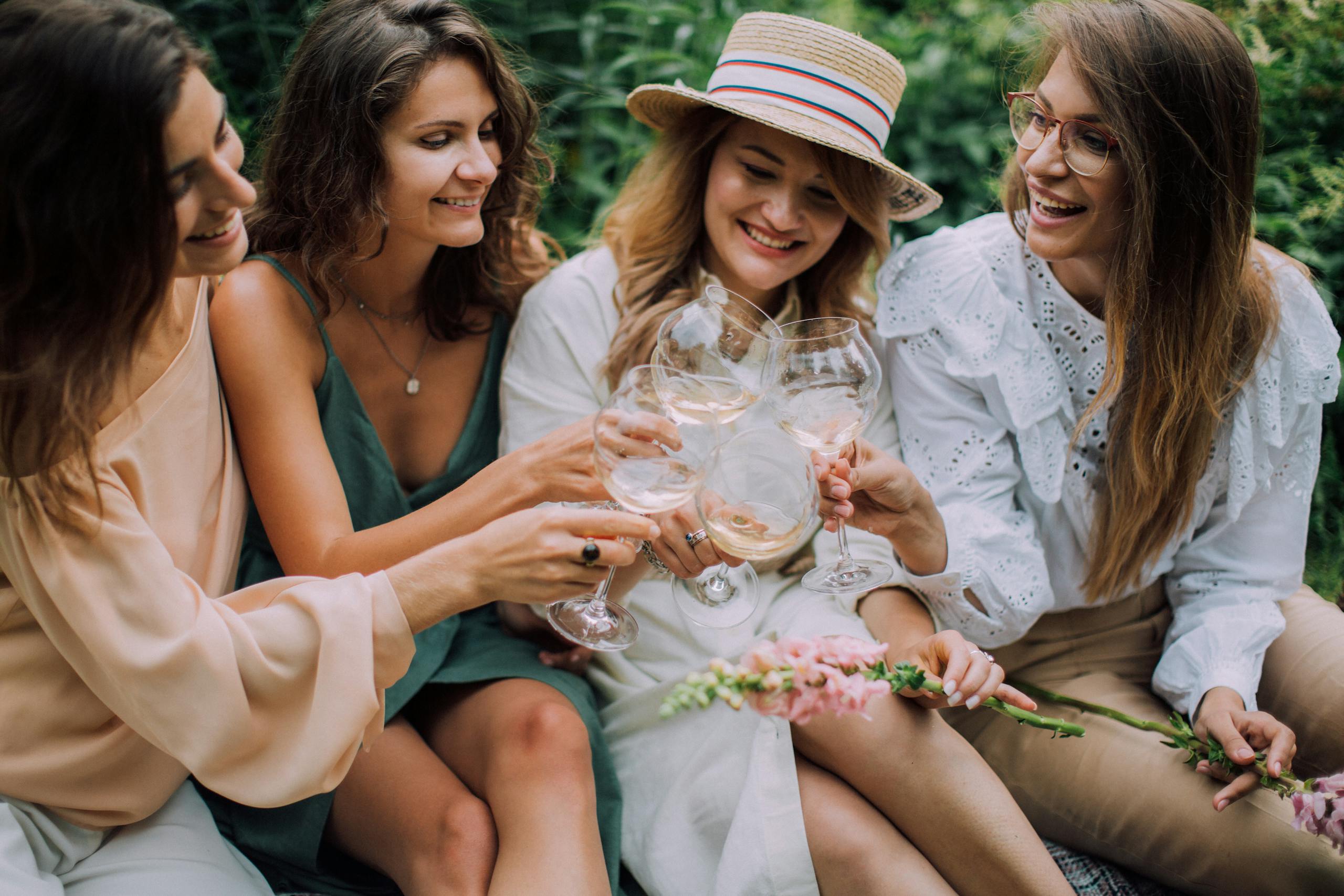Four women celebrating with white wine outdoors, smiling and enjoying a summer day.