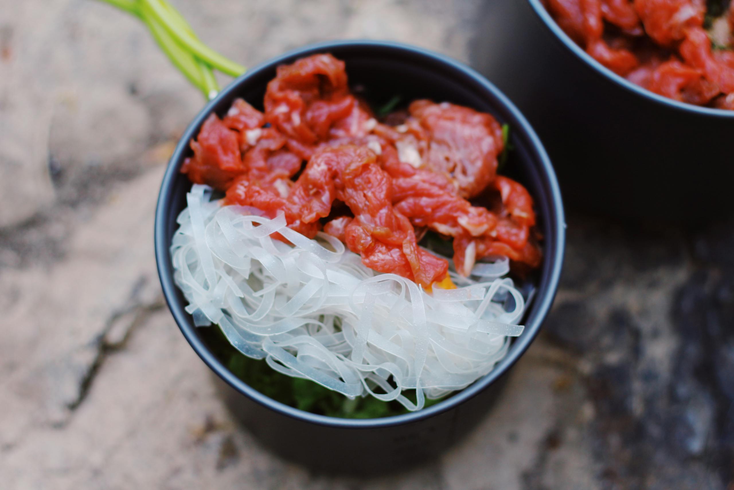 From above of bowl with rice noodles and red raw meat placed on blurred background