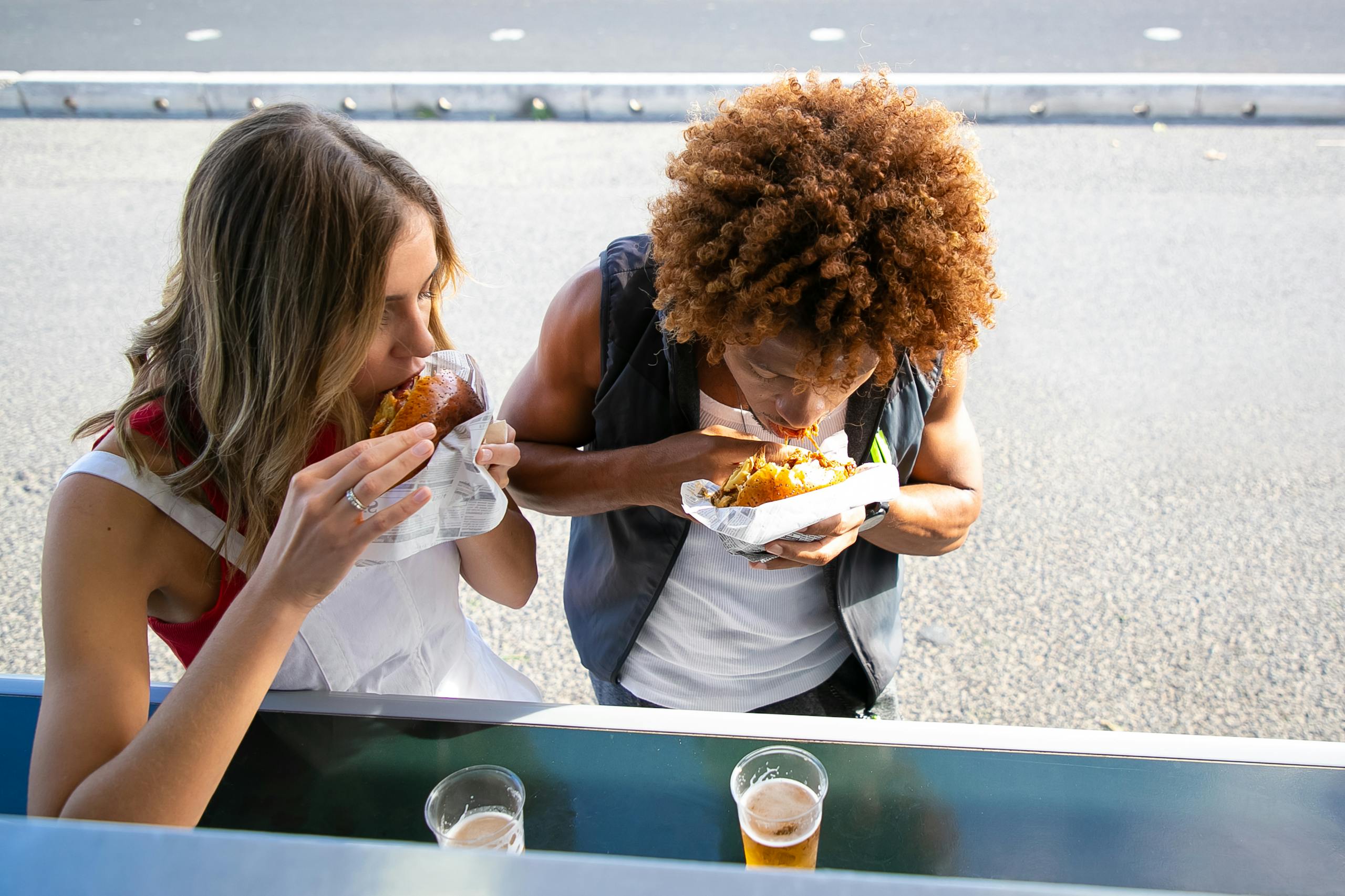 From above of diverse couple eating tasty burgers with roast chicken and having beer at counter of food truck