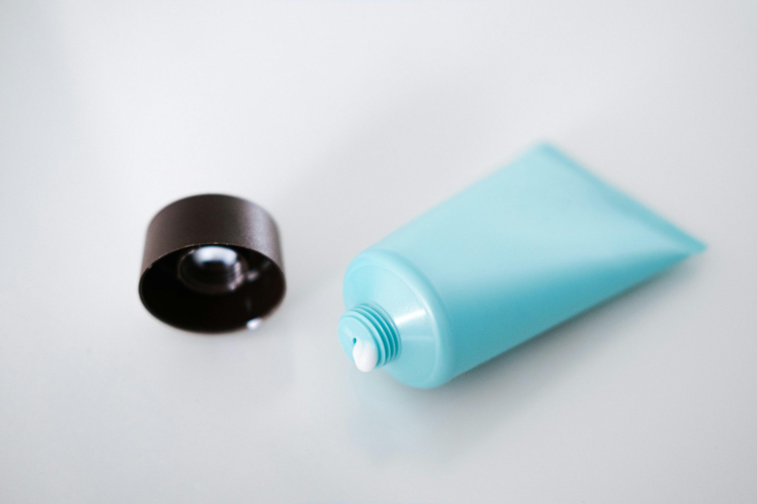 From above of open shiny tube of nourishing cream with lid on light background