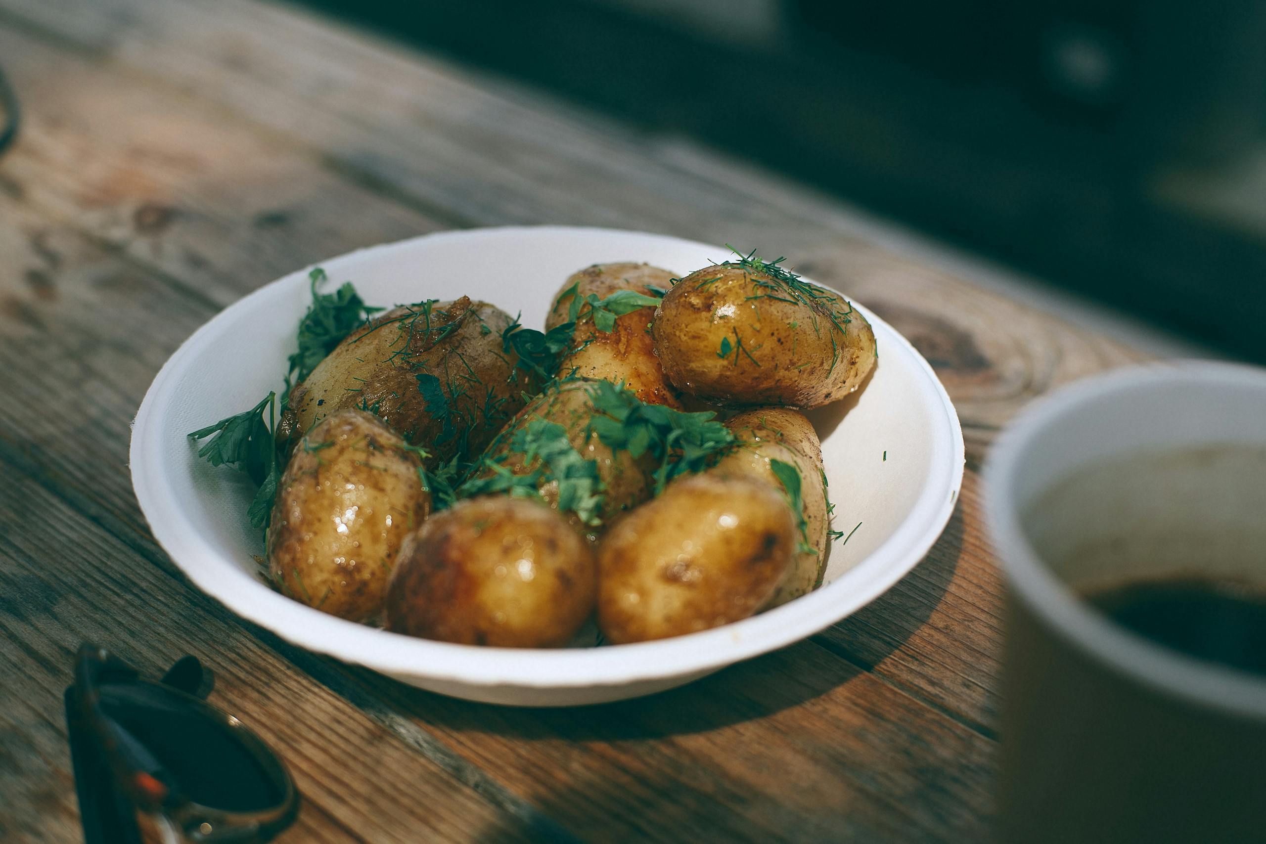 From above of tasty appetizing roasted potatoes with greenery in white plate on wooden table