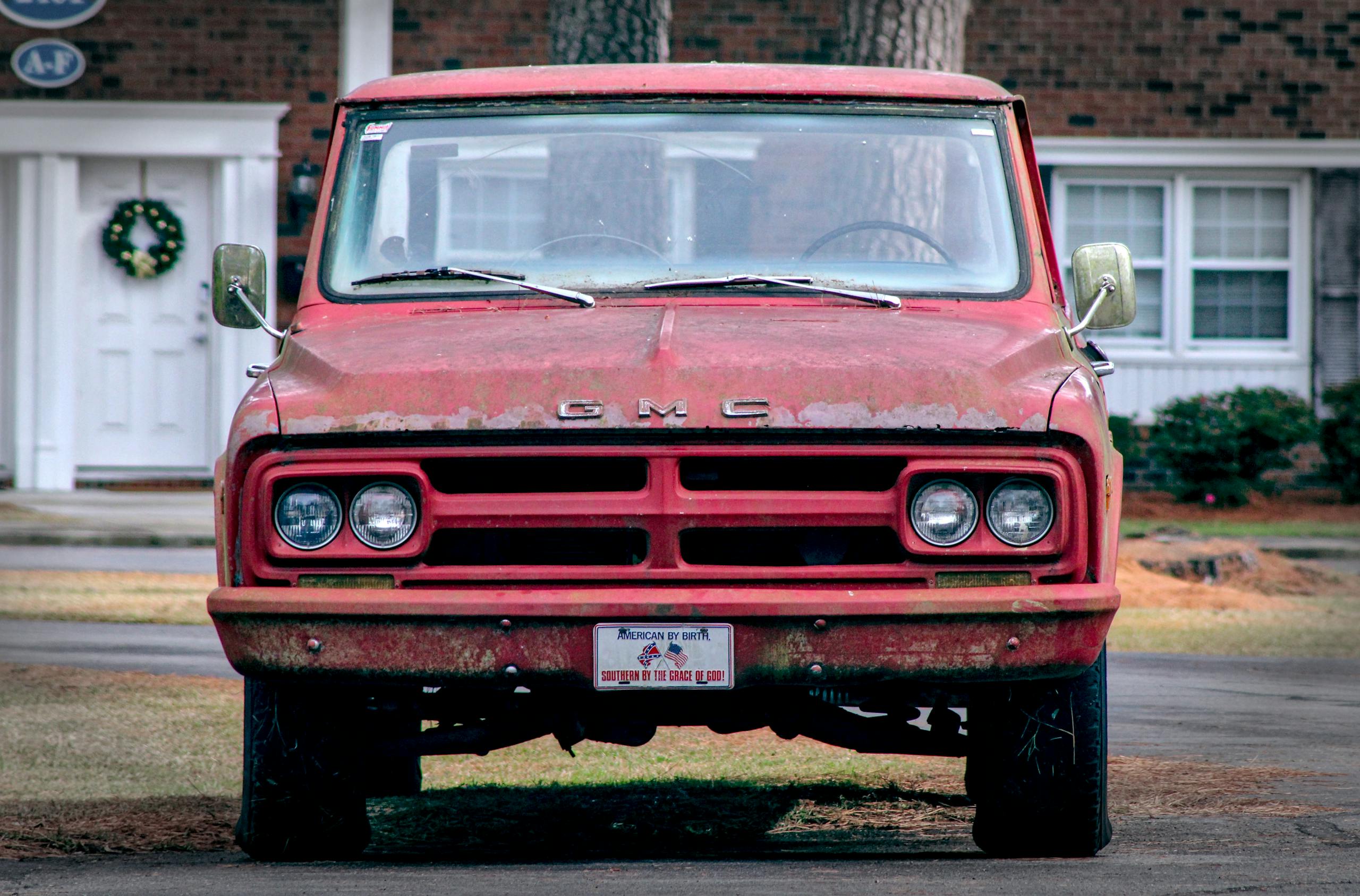 Front view of a classic red GMC pickup truck parked on a suburban street with a festive wreath on a nearby door.
