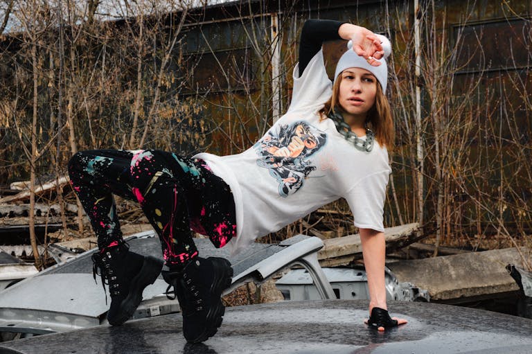 Full body of serious young female in activewear and hat dancing hip hop on abandoned car roof on autumn day